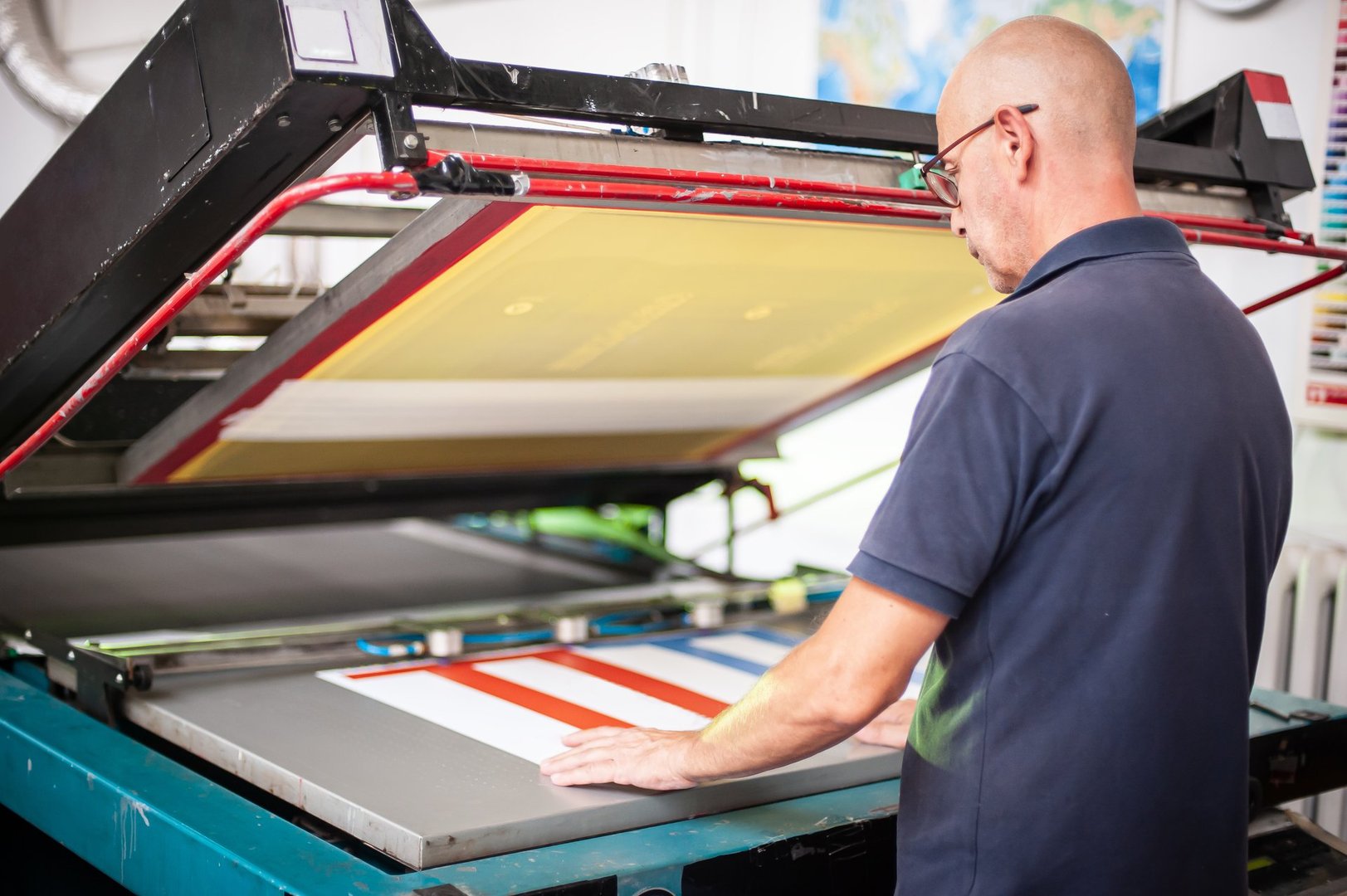 In the printing house, an experienced technician works on a screen printing machine. Production work. Check the print quality.
