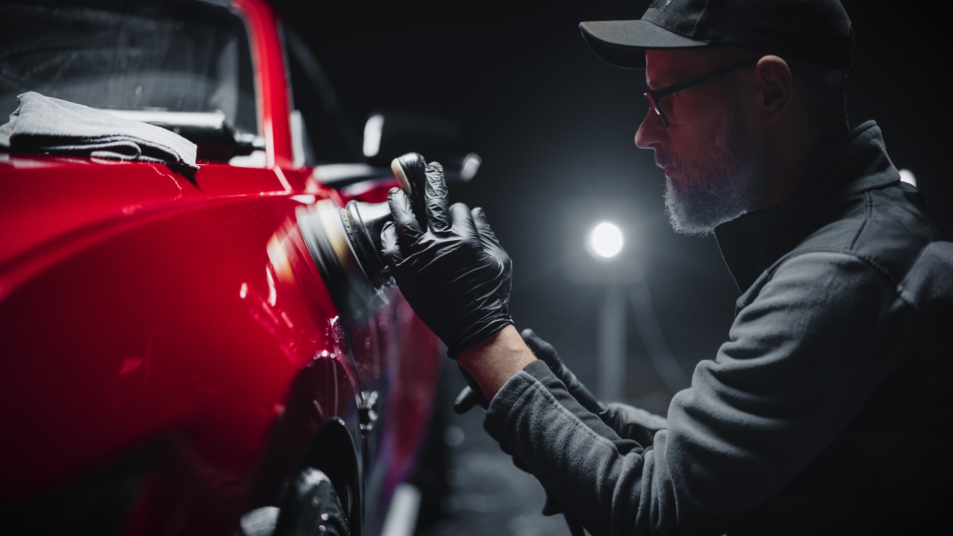 Red Sportscar Standing in a Stylish Detailing Dealership Studio. Professional Worker Buffing the Body from Light Scratches, Removing Swirls and Paint Defects from a Fender of the Vehicle