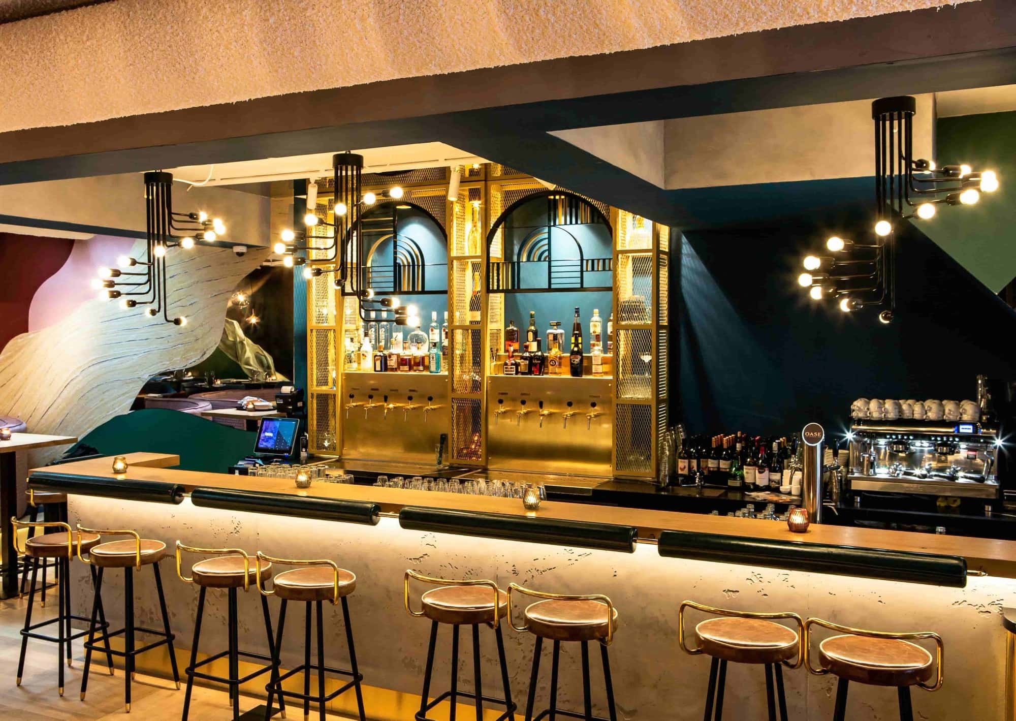 Modern bar interior with a long counter, stools, and illuminated shelves with bottles. Stylish lighting and decor.