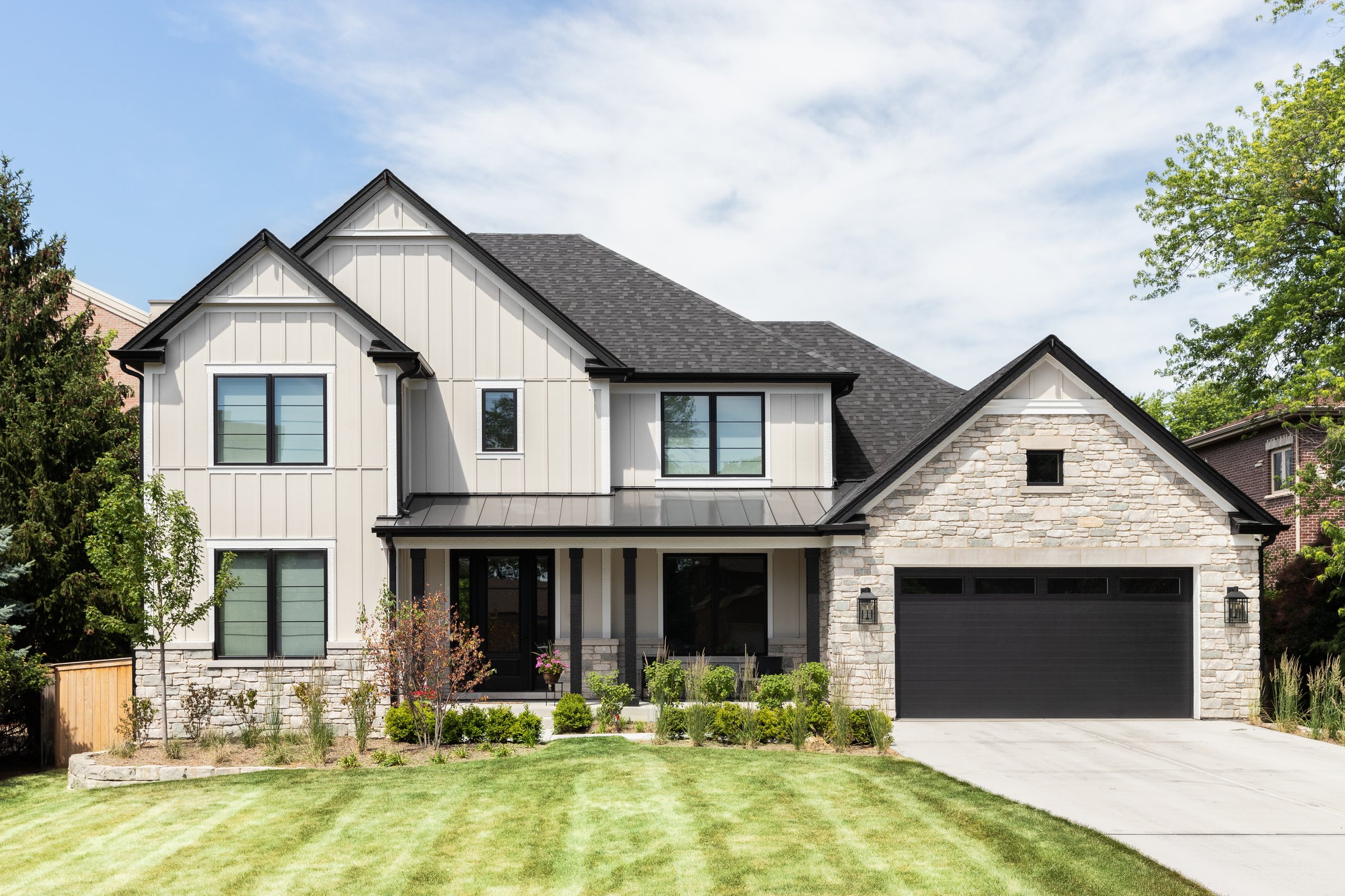 Oak Park, IL, USA - May 30, 2022: A tan modern farmhouse with a wainscoting siding, covered front porch, beautiful landscaping, and stone covered garage.