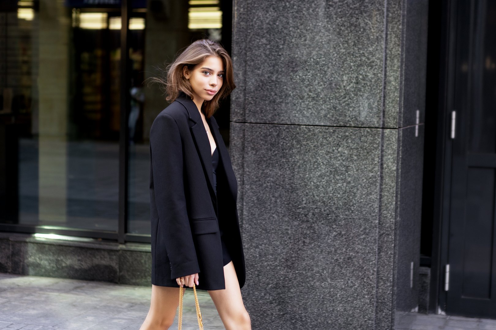 Fashionable young woman wearing elegant outfit oversize black blazer, beautiful model with dark hair Walking urban city. Modern fashion, street style