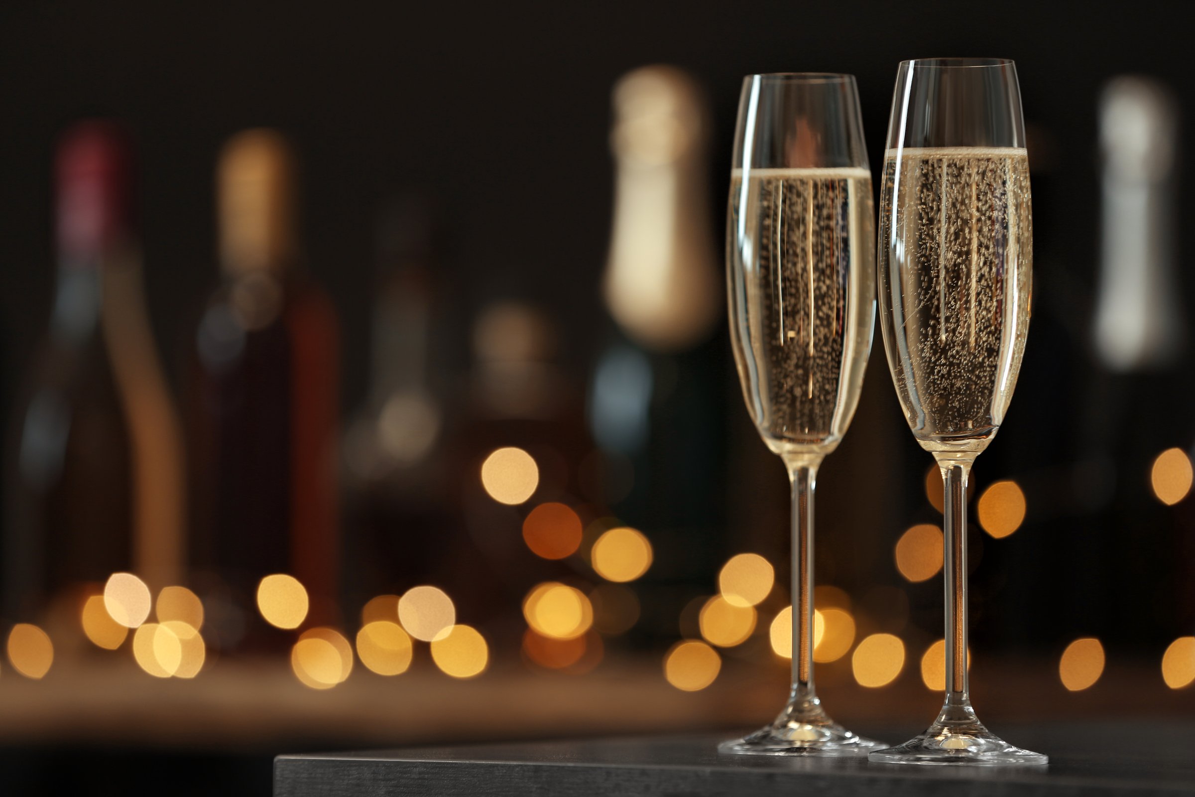 Two glasses of champagne in a dimly lit room with blurred bottles in the background for celebrations. Great for parties and special moments.