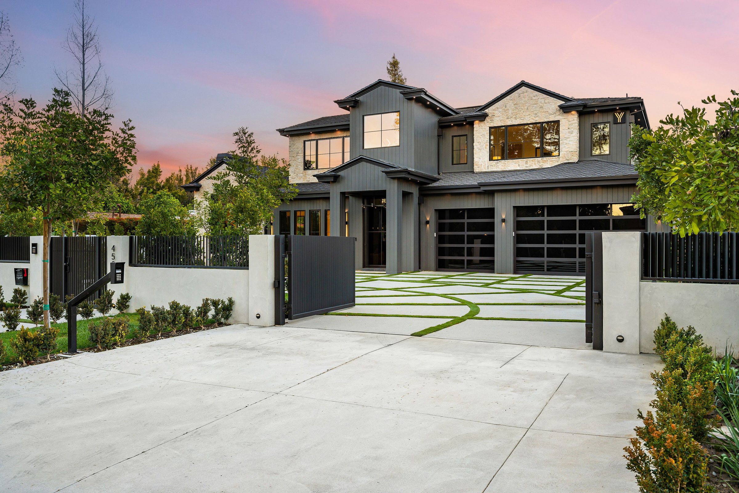 Modern luxury home with a sleek exterior design, landscaped driveway, and sunset sky in the background.