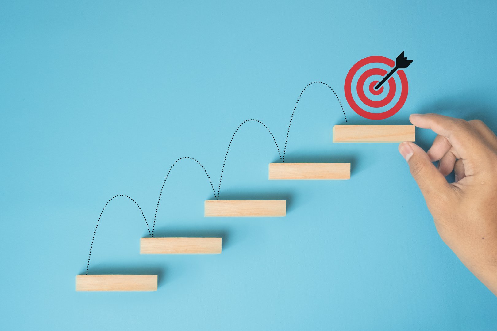 Male hand arranges a wooden block staircase with target icon. Achieving goals and objectives or goal setting