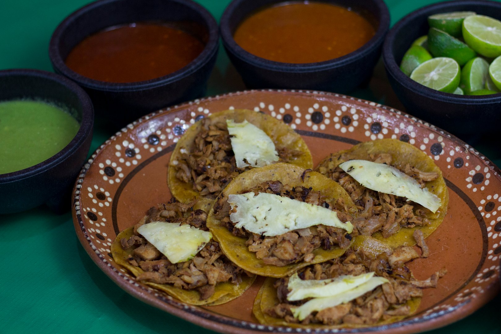 A vibrant plate of mouthwatering tacos topped with cheese, surrounded by colorful salsas, fresh limes, and a rich green backdrop, perfect for food enthusiasts.