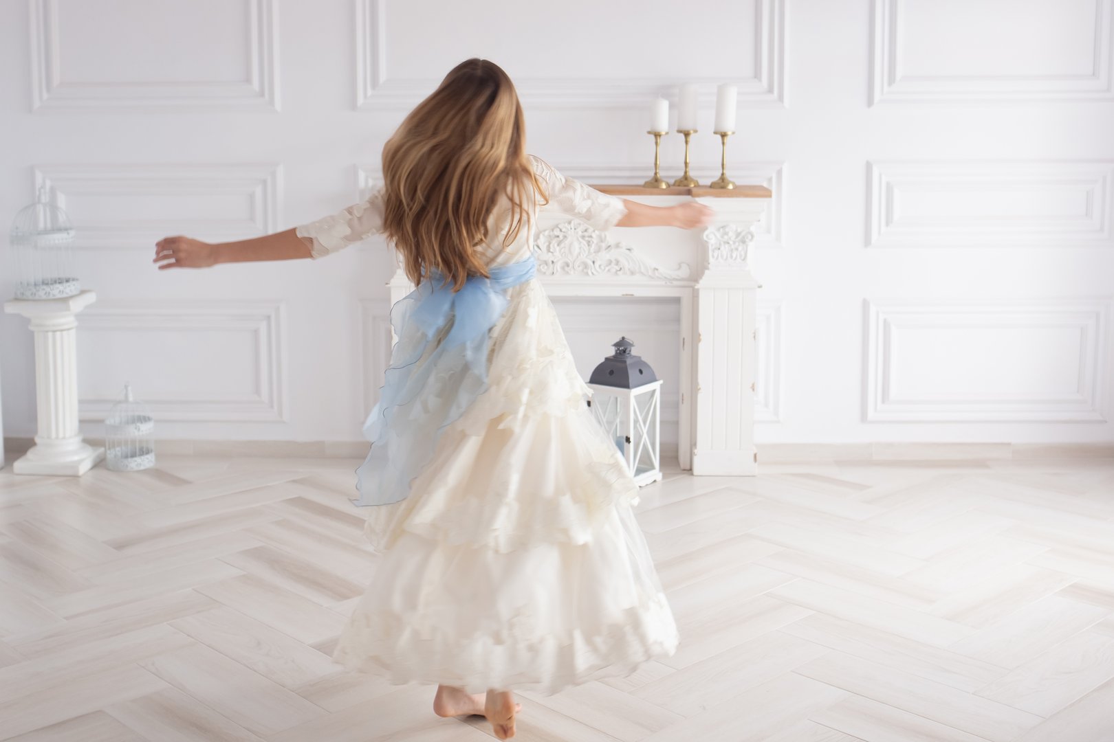 A happy girl in a smart white dress dances and twirls in a large bright living room at her first communion.