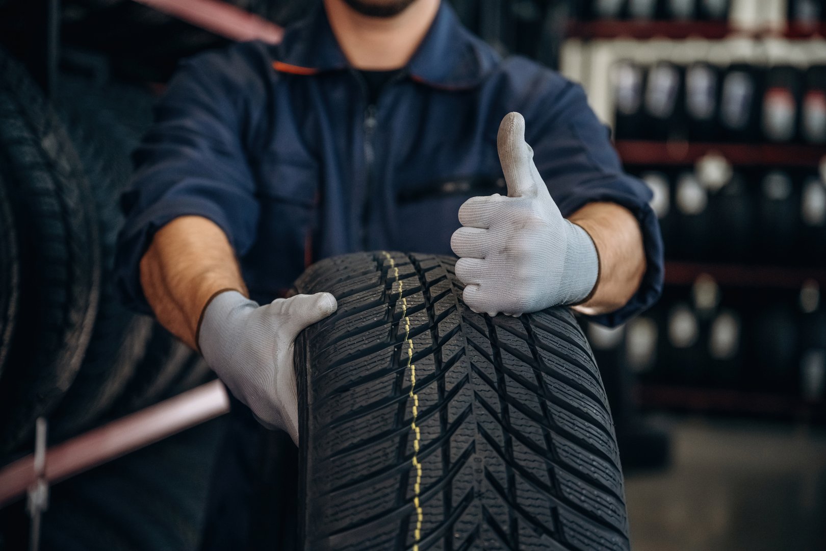 Focused close up view, thumb up, holding a tire. Man worker is maintenance station with wheels.