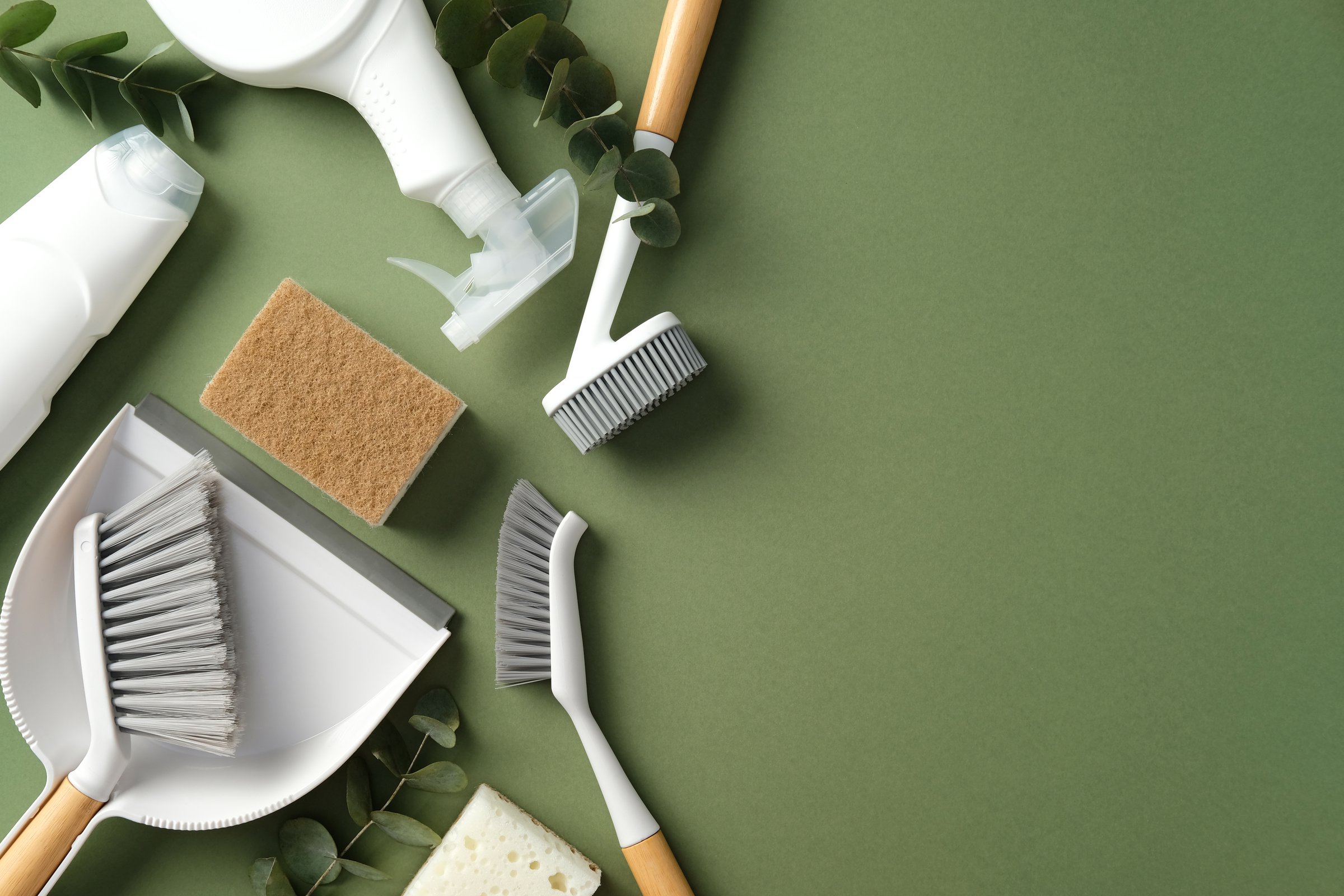 Cleaning supplies on a green background, including brushes, a dustpan, sponges, and spray bottles. Perfect for illustrating household cleaning themes.