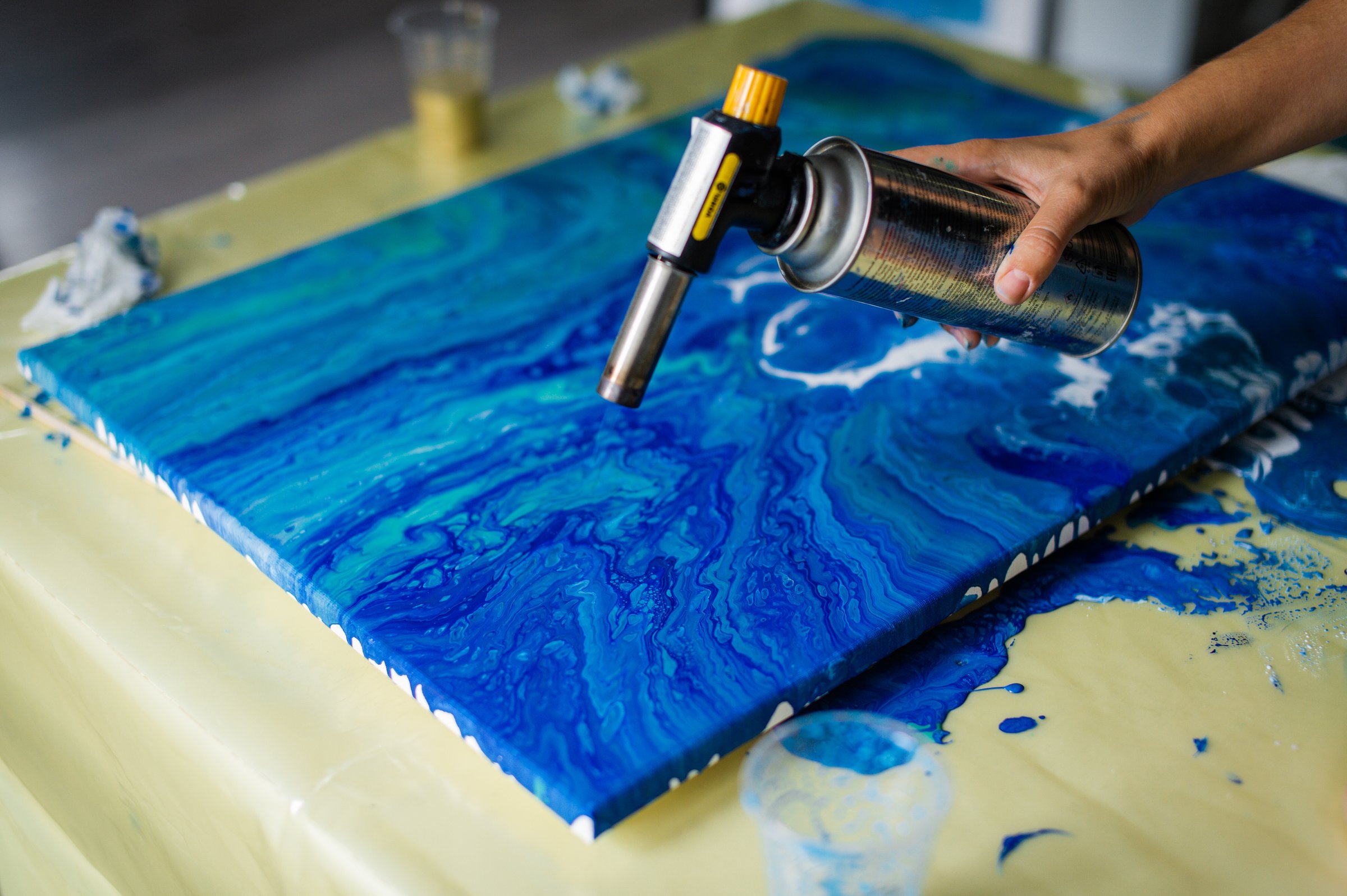 Artist's hand using a heat gun on a blue epoxy resin art piece