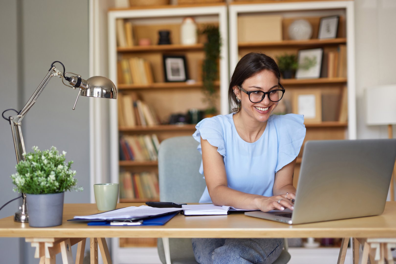 Smiling young woman working from home, typing on a laptop and looking at the screen