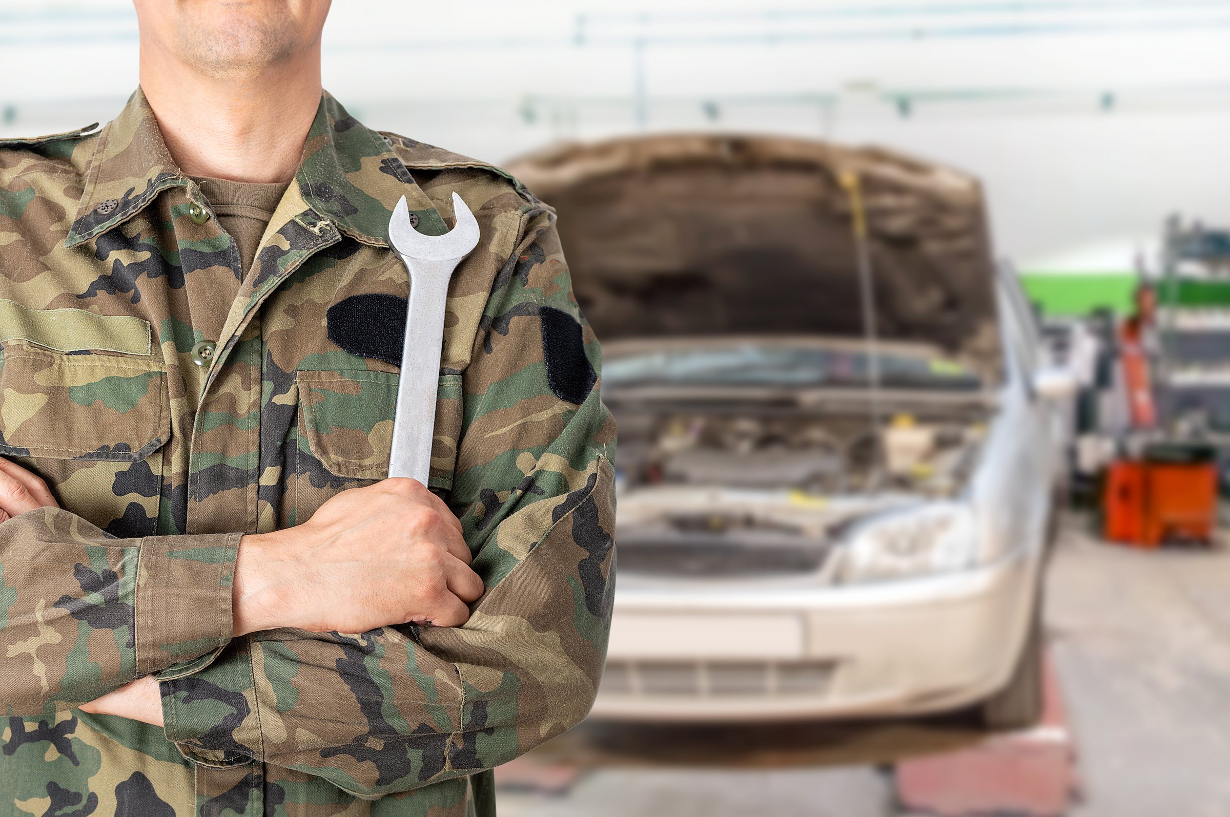 Hand of a military car mechanic with wrench. Car repair garage.