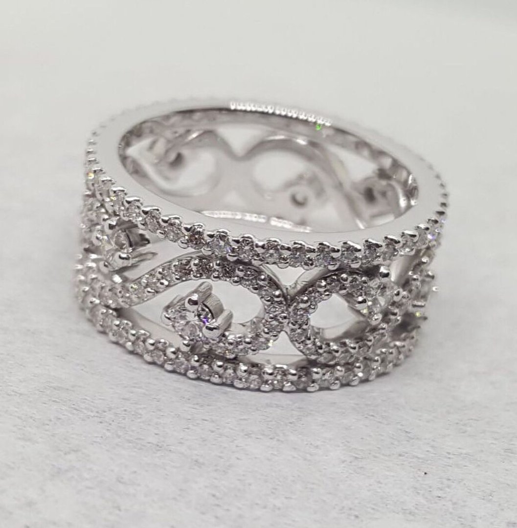 Silver ring with intricate swirl design and embedded small clear gemstones on a light background.