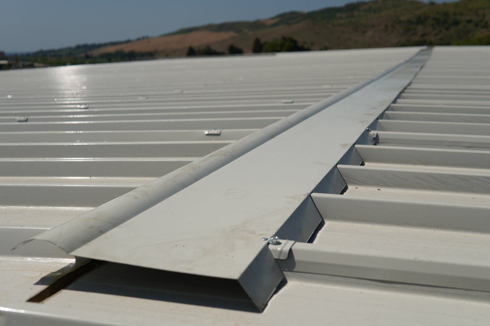 Installation of a specialized ridge cap designed specifically for industrial white sandwich panels. The ridge cap is attached with rivets and sealant to ensure strength and water resistance.