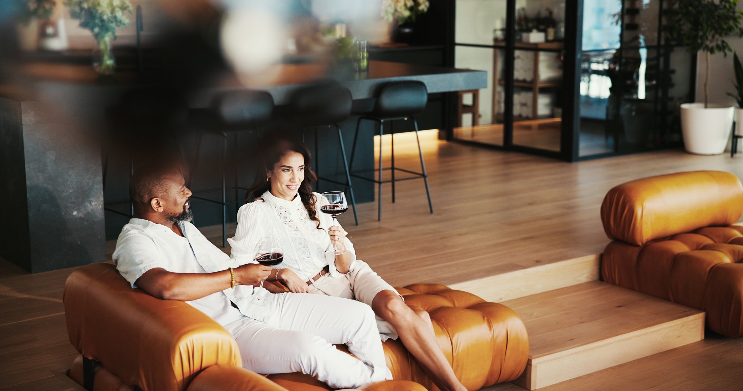 House, red wine and couple on sofa, relax and comfort with break, bonding together and romantic. People, apartment and man with woman on couch, alcohol and conversation with relationship in lounge