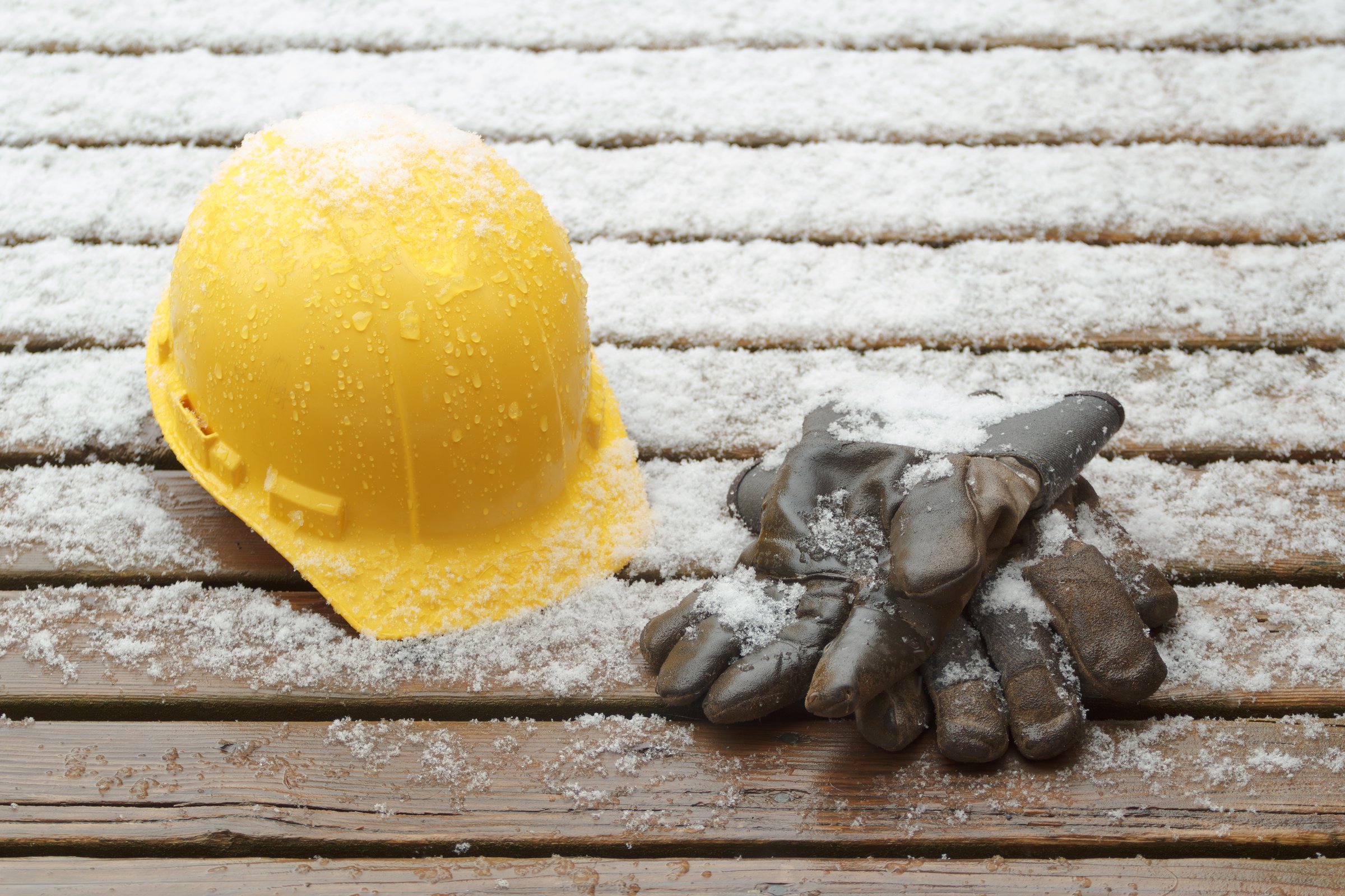 Hard hat and work gloves on wet deck boards with light snow