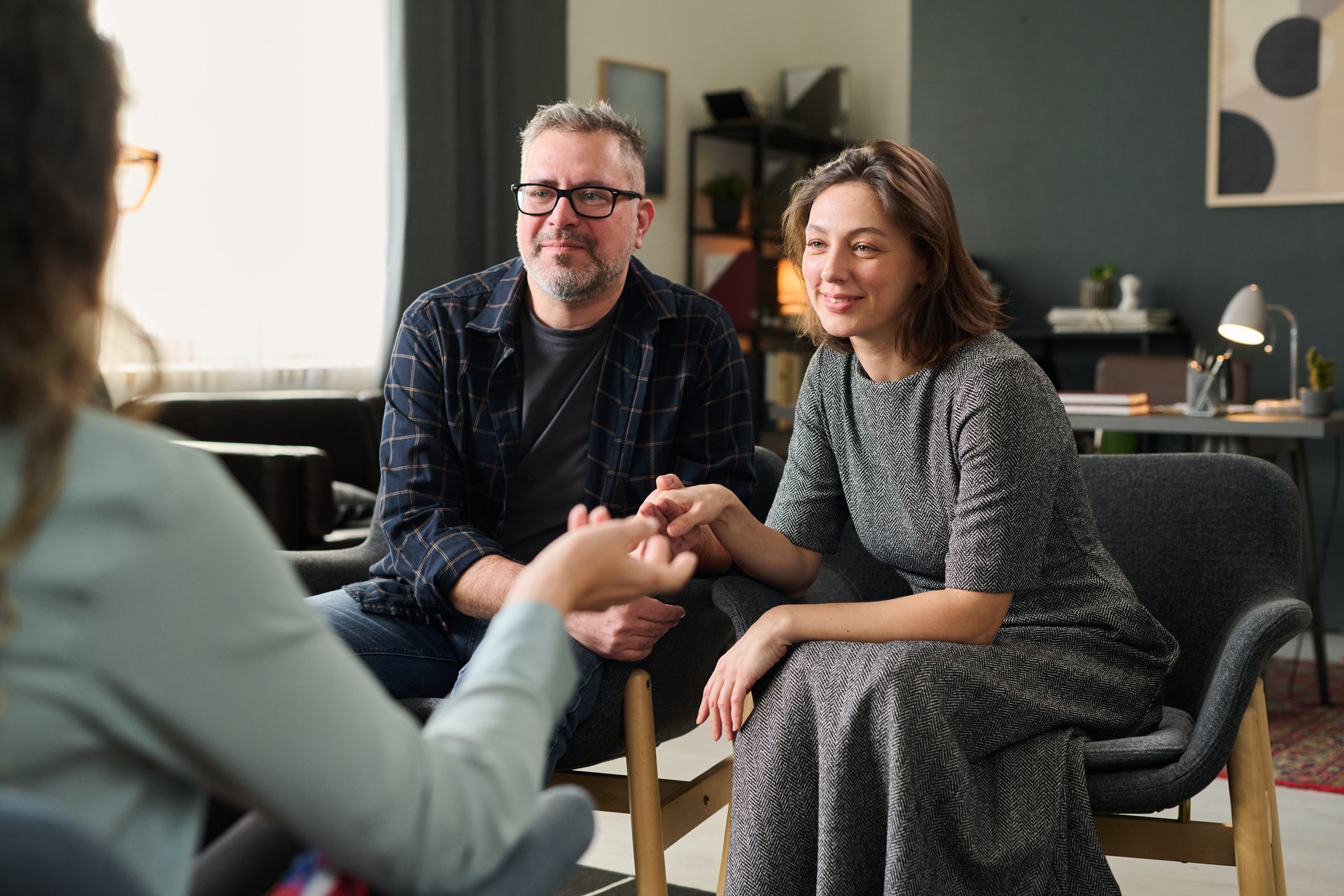 Couple sitting close together attentively listening to a counselor in cozy and well-lit room holding hands creating an intimate and empathetic atmosphere