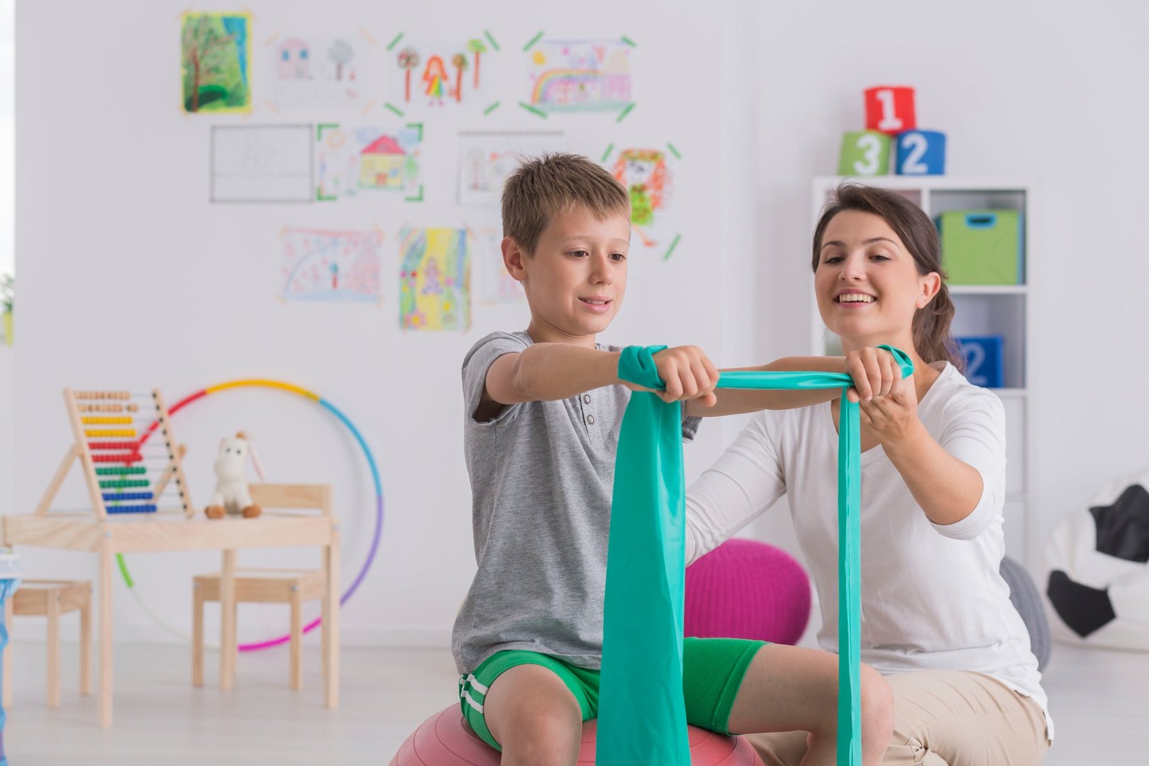Physiotherapist and boy sitting on a gym ball exercising with a rubber tape