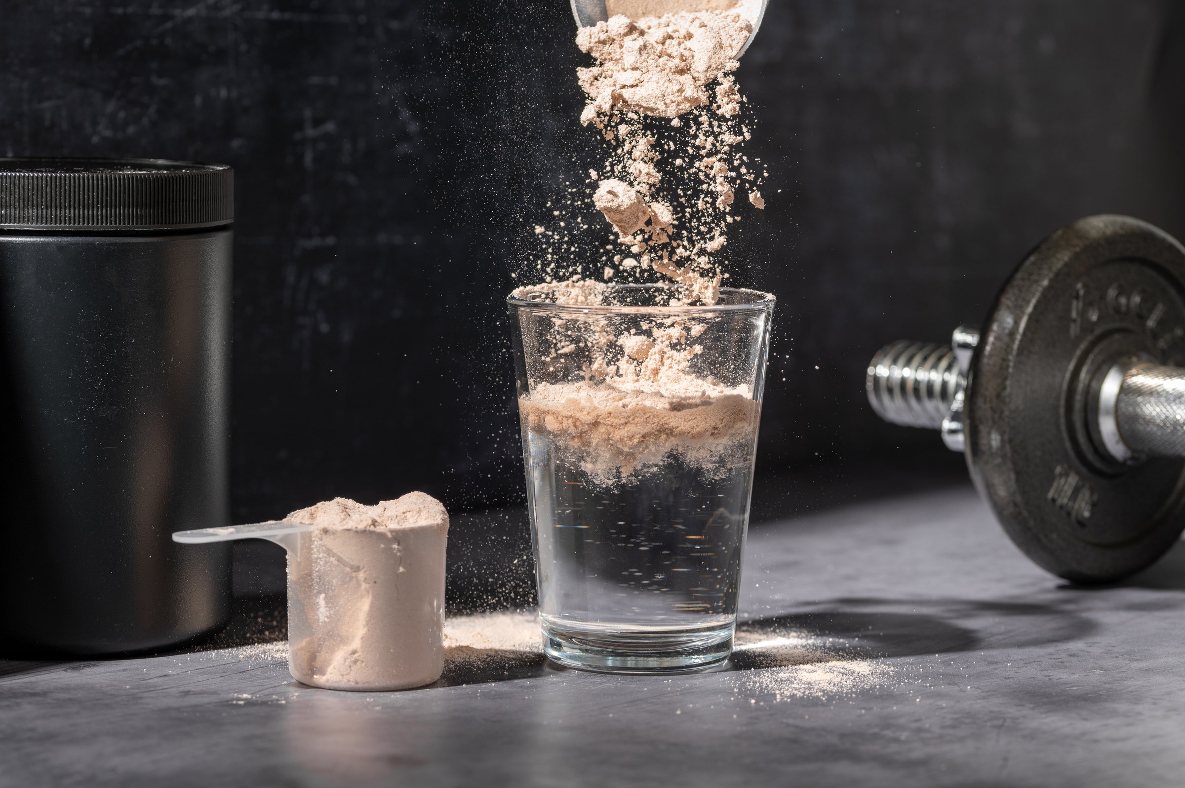 Pouring Chocolate protein powder in a glass. Food supplements. Dark background. Bodybuilding, fitness, gym
