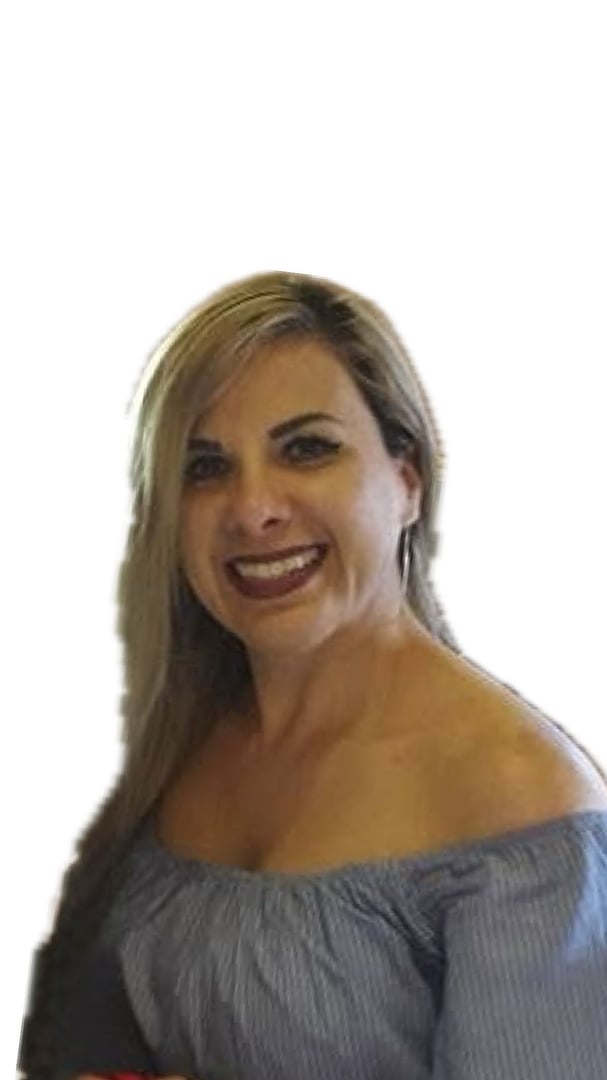 A woman smiling, with long blonde hair, wearing an off-shoulder blue top against a plain background.