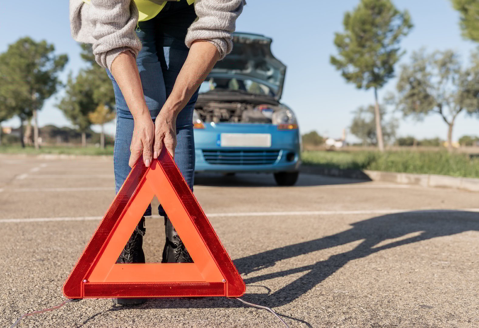 Woman placing reflective warning triangle on road near broken down car with open hood