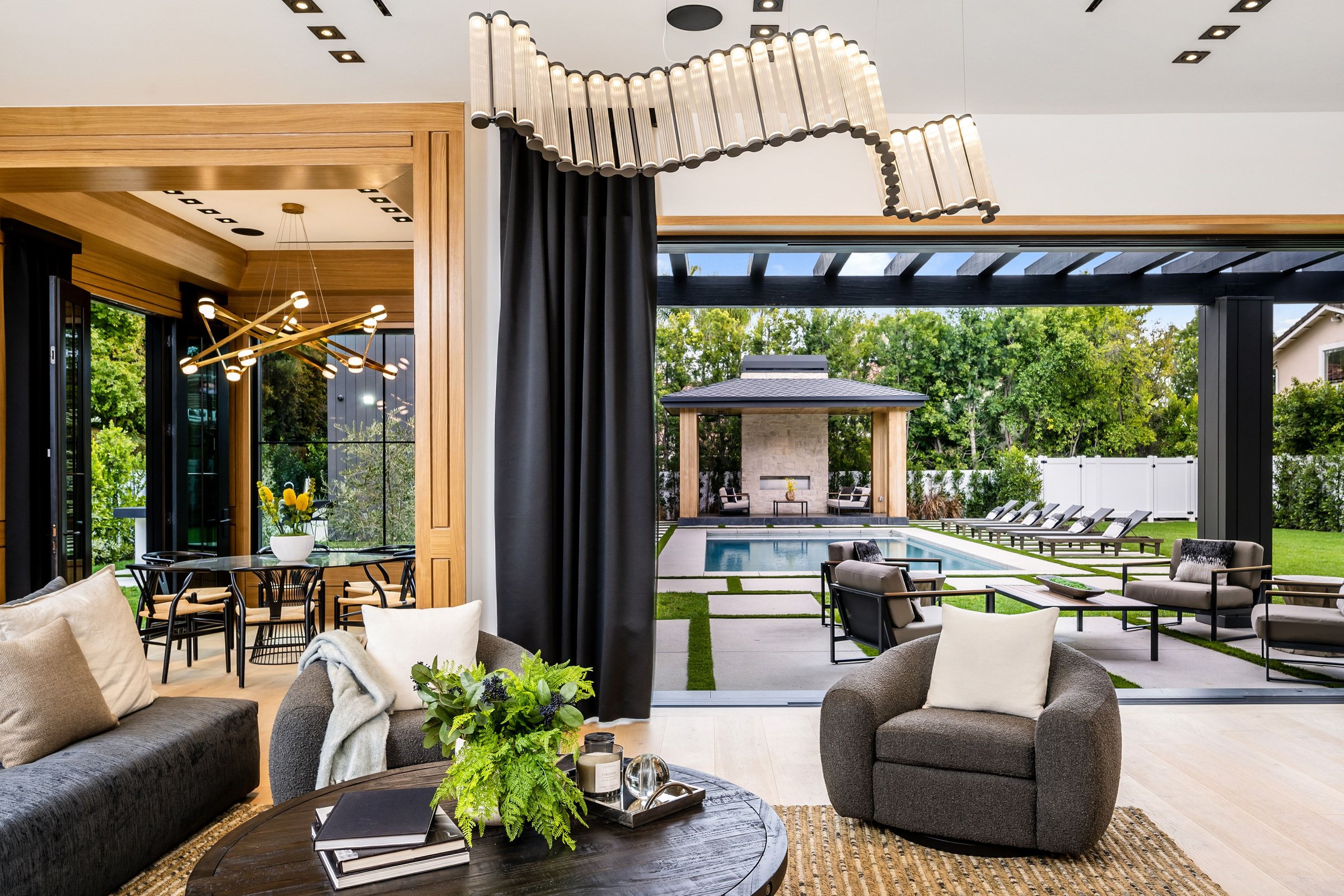 Modern luxurious living room with a view of a stylish outdoor pool area and garden, featuring contemporary furniture and elegant lighting.