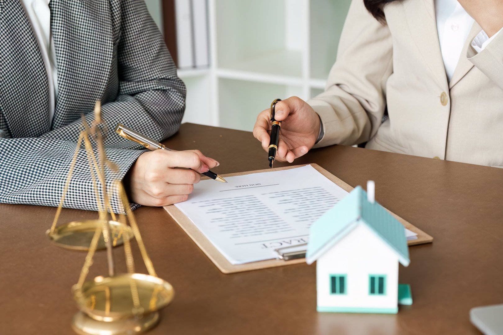 Two lawyers discussing and reviewing legal documents with scales of justice and a house model on the desk, symbolizing law and real estate.
