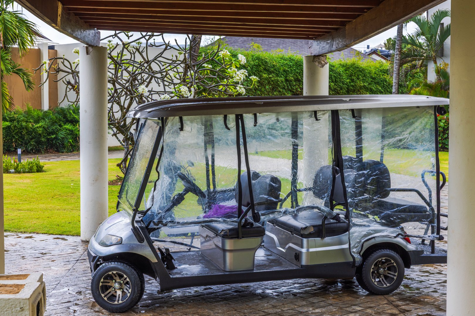 Electric golf cart with rain covers parked under roof at tropical resort during wet weather. Punta Cana. Dominican Republic.