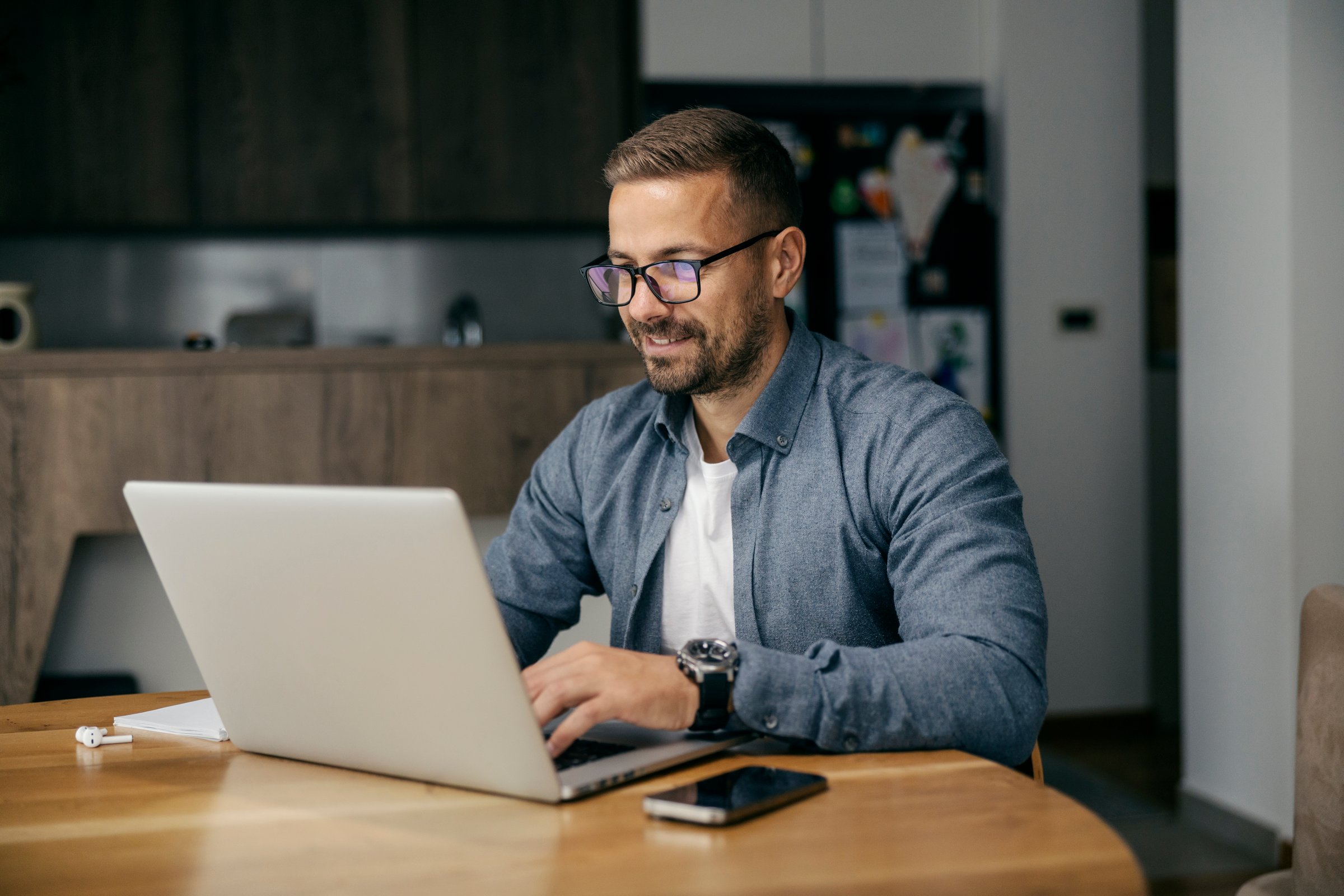 Smiling man working on laptop at kitchen table