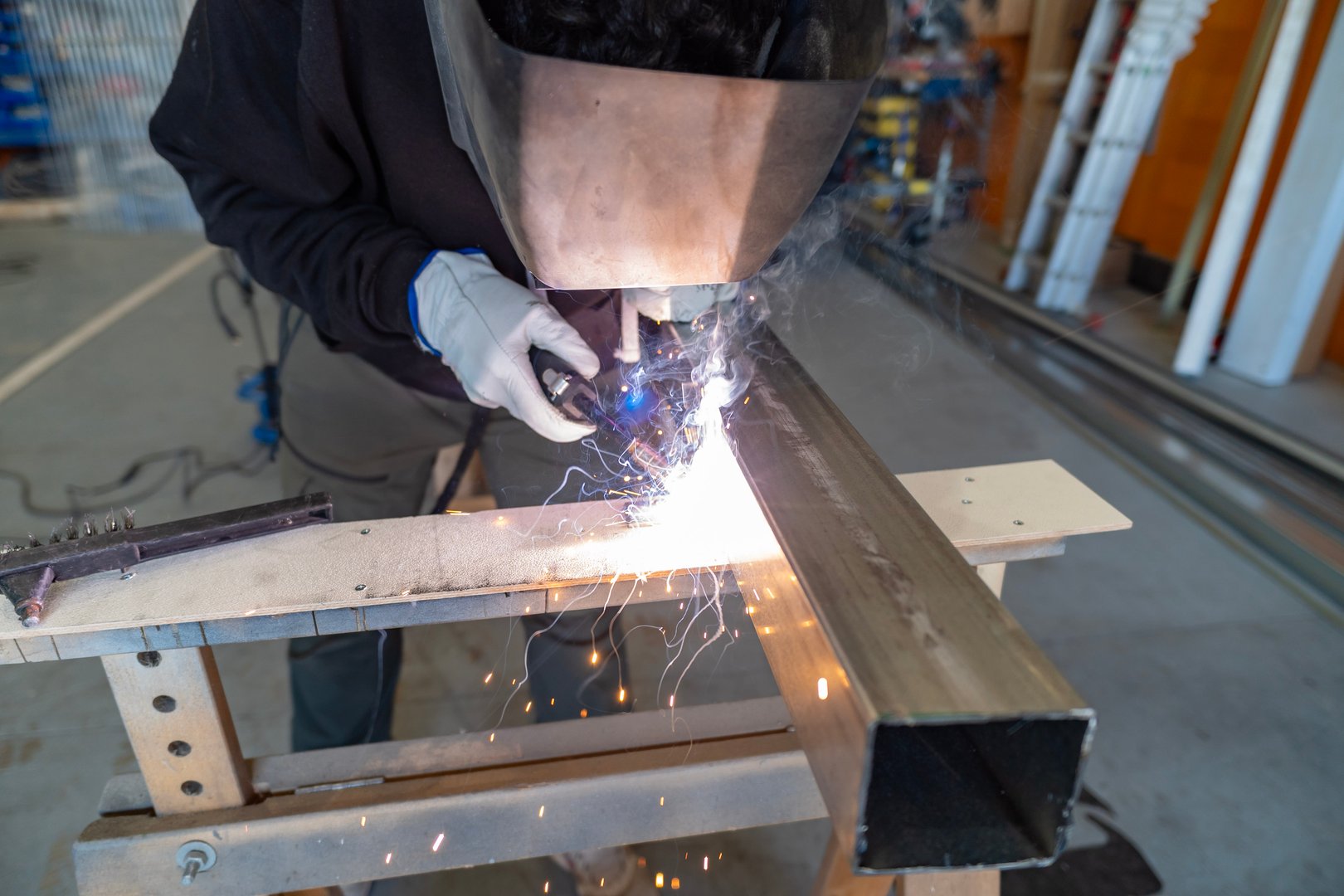 Person wearing protective helmet and gloves welding metal in a workshop