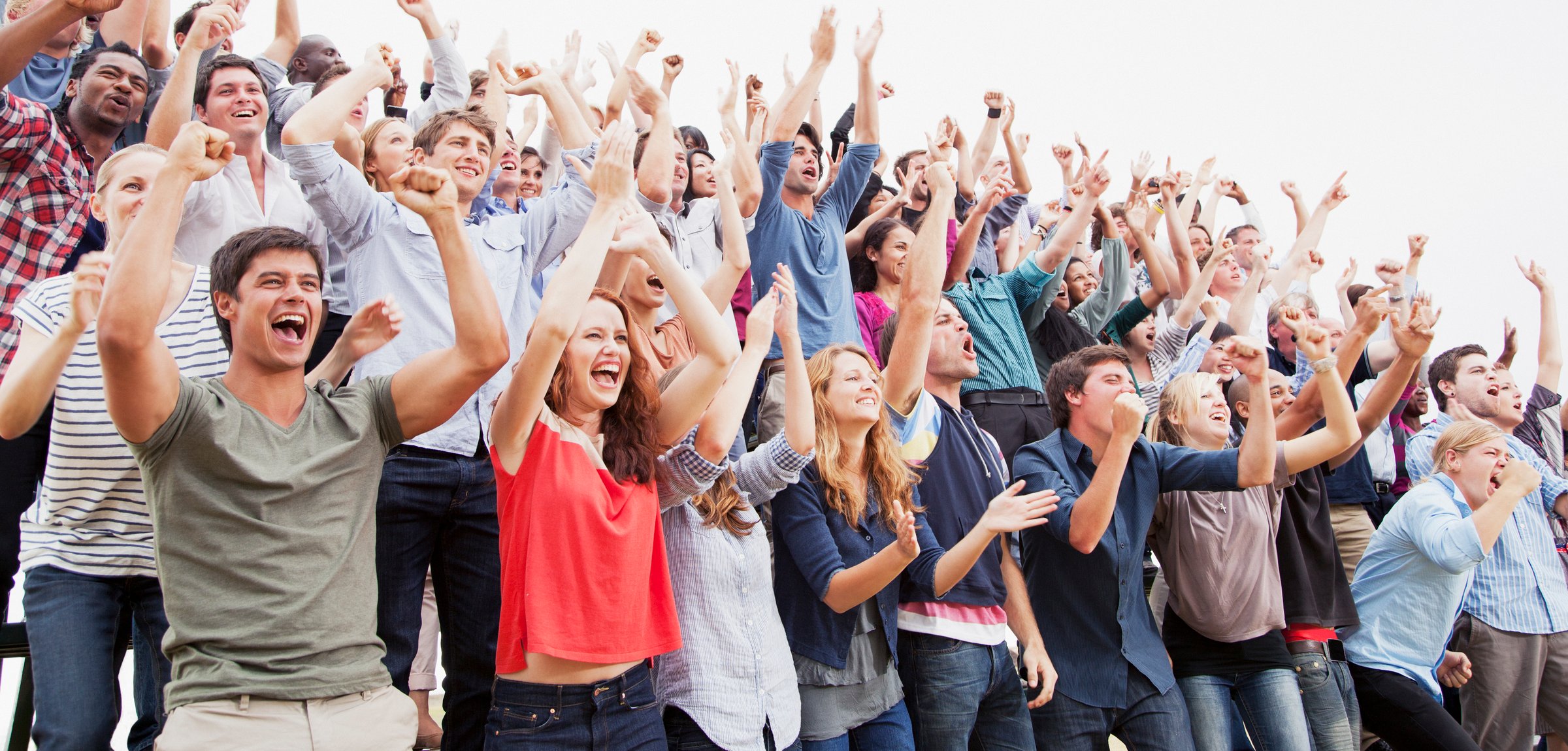 A large, diverse group of enthusiastic people cheering and raising their fists in the air, indicating excitement and celebration.
