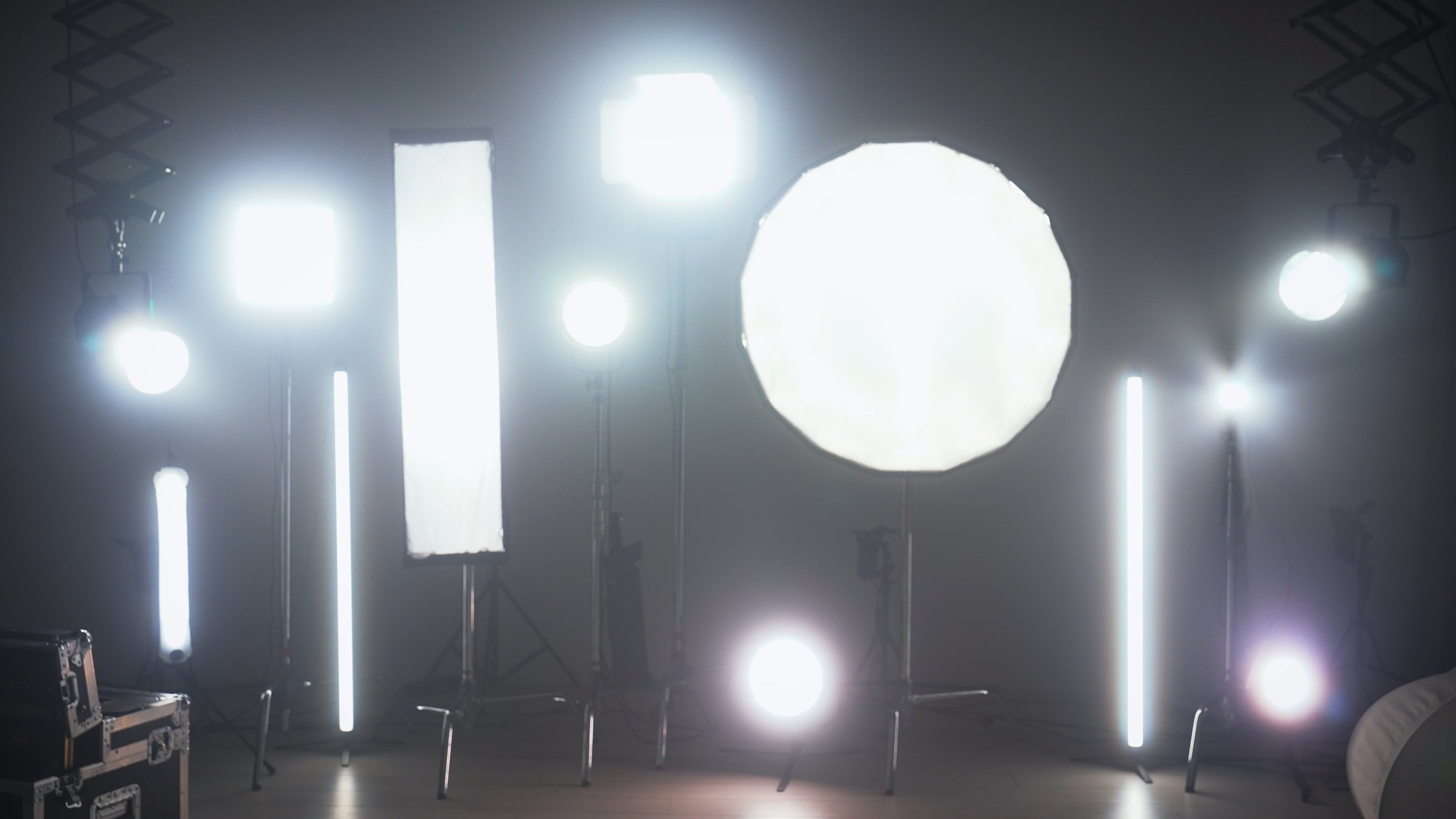 Multiple studio lights, softboxes, and LED panels illuminating a film set. Equipment includes vertical tubes, octaboxes, and overhead lighting mounts. Backstage preparation for studio professional shooting.