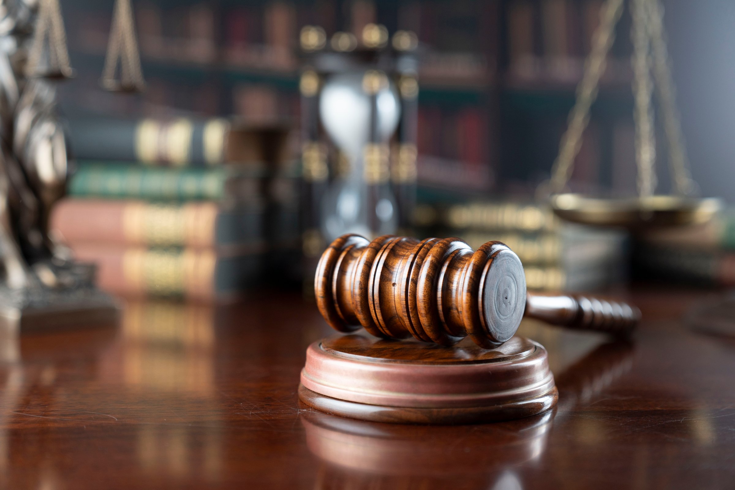 Law symbols on library background. Gavel, wooden table, books, statue of justice.