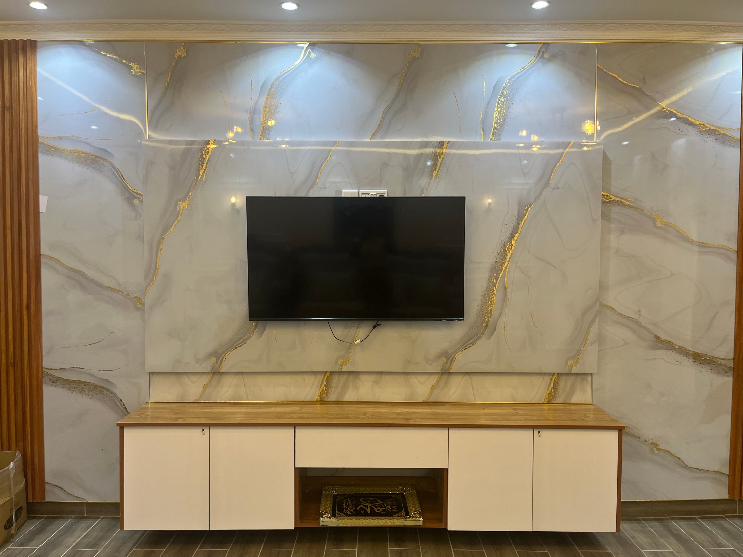Modern living room with marble accent wall, mounted TV, and wood-cabinet console beneath, featuring golden veining design.