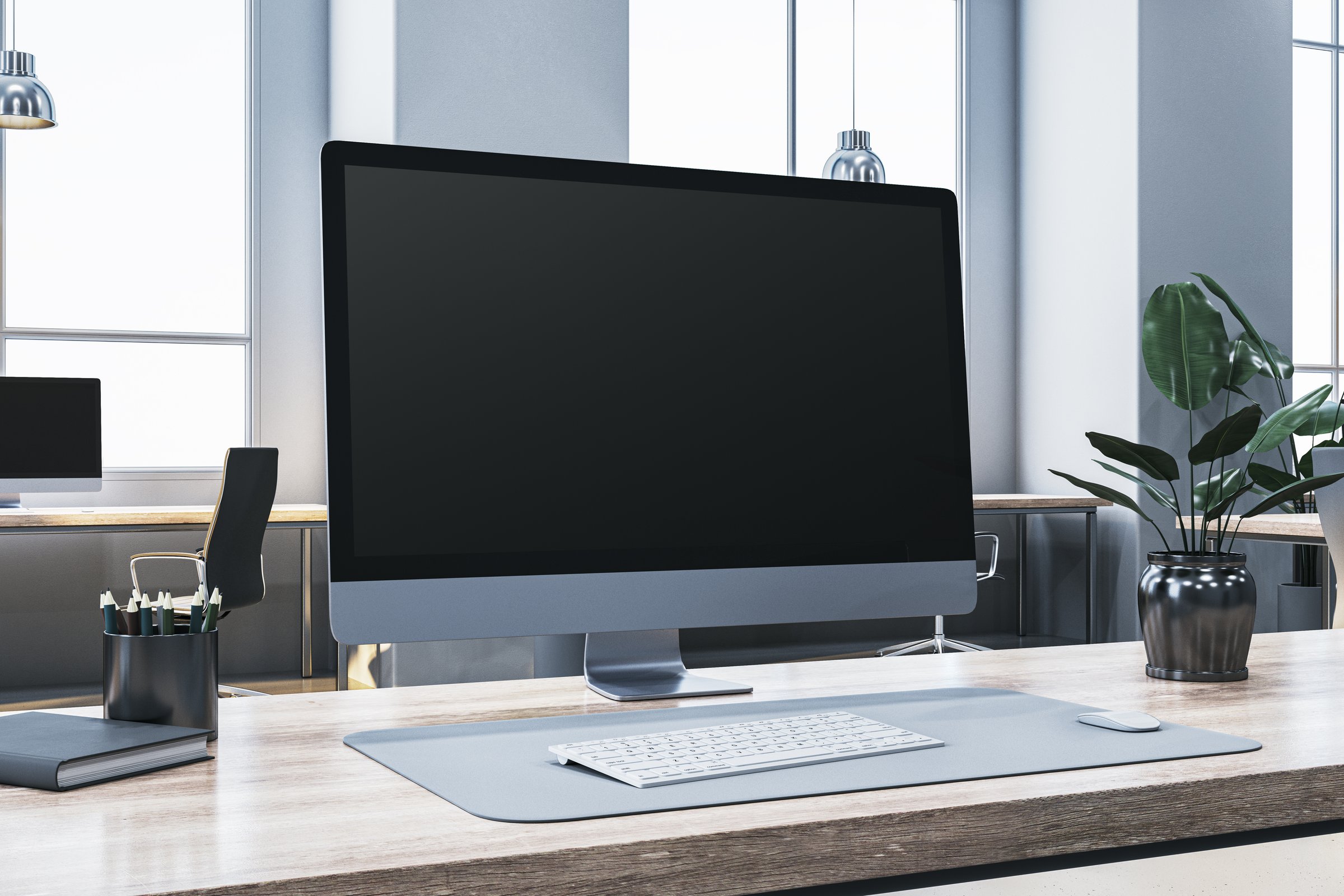 A modern desktop computer monitor on a wooden office desk, placed in a bright office environment with large windows, representing technology and business. 3D Rendering
