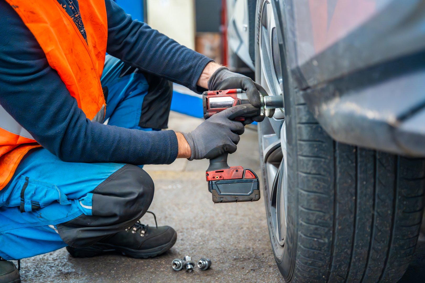 Mechanic using an impact wrench to remove lug nuts from a car wheel. Seasonal tire change and professional car service in preparation for winter. High quality photo