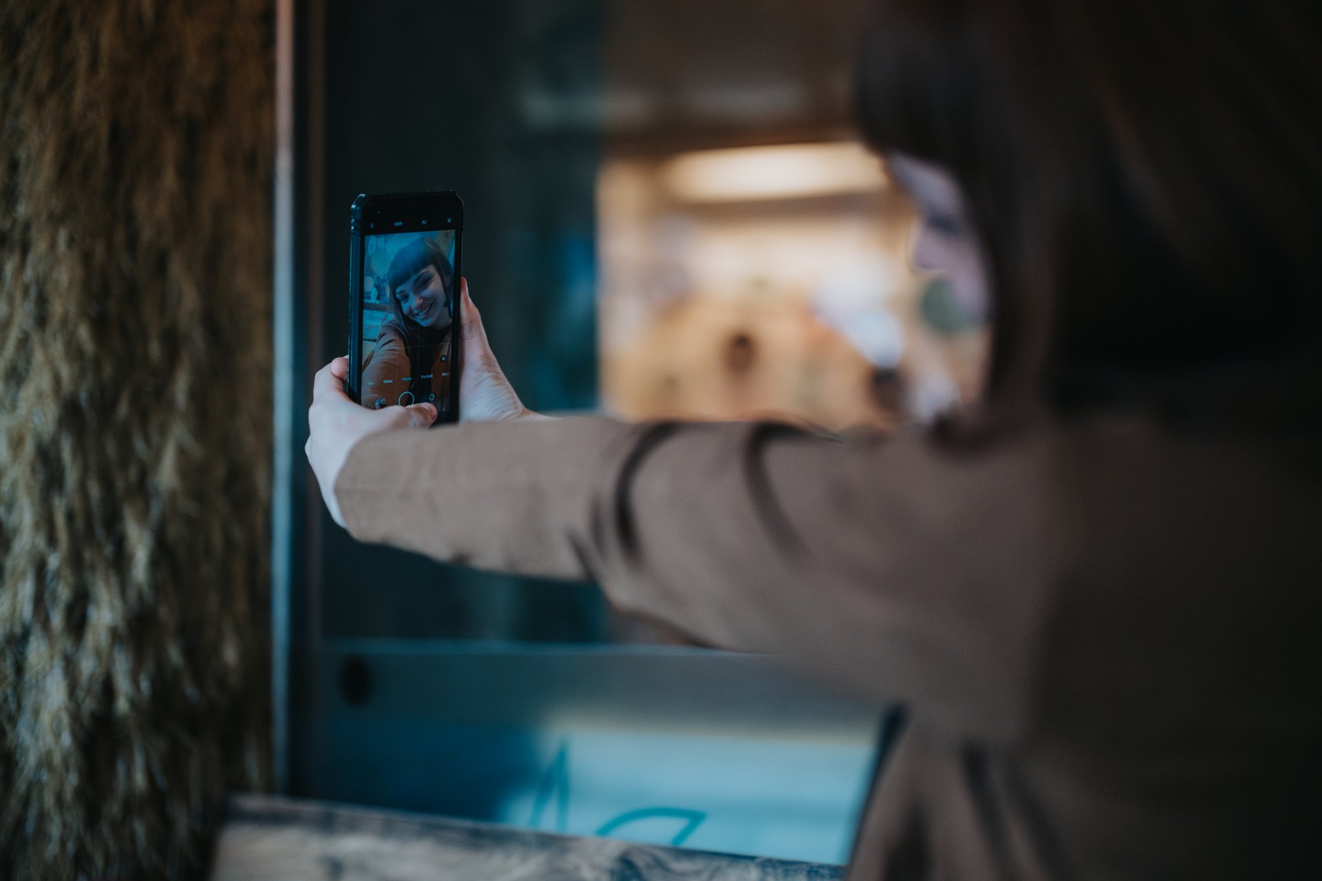 A young woman is taking a selfie with her smart phone indoors, showcasing a candid and lively moment.