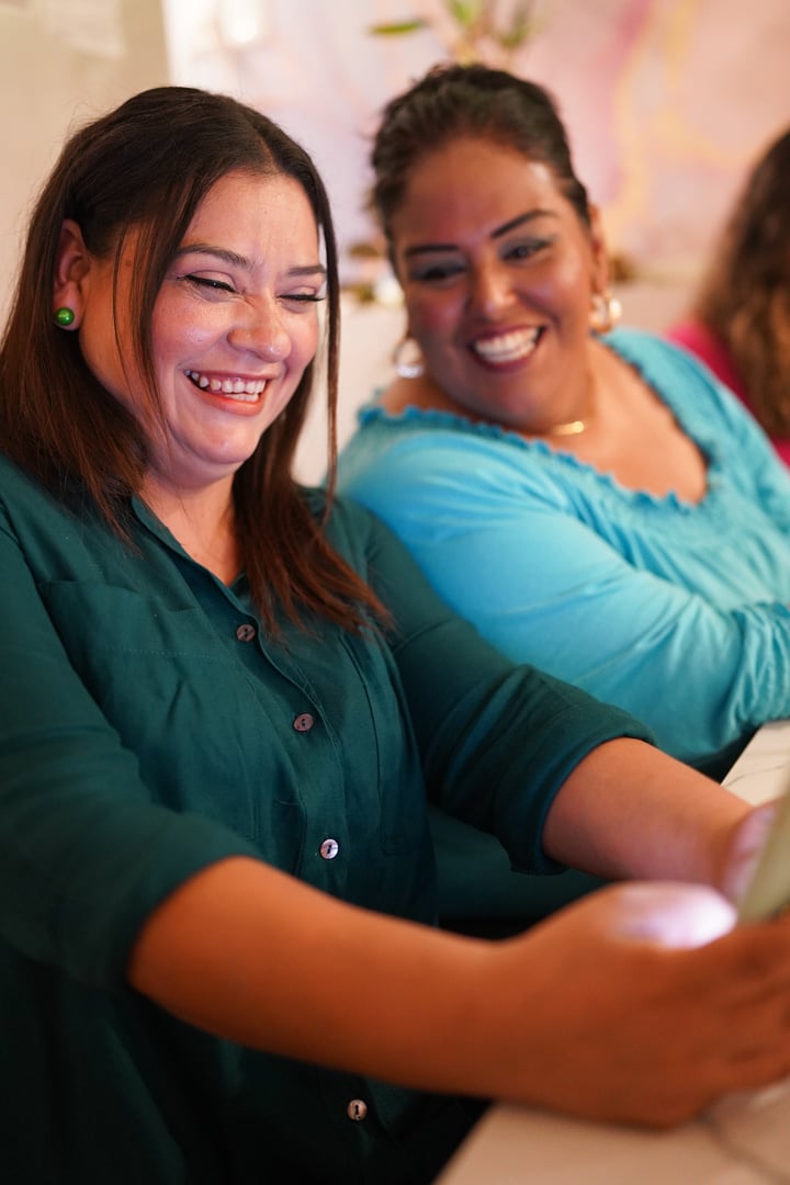 Two latin women entrepreneurs are smiling and using a smartphone for online sales