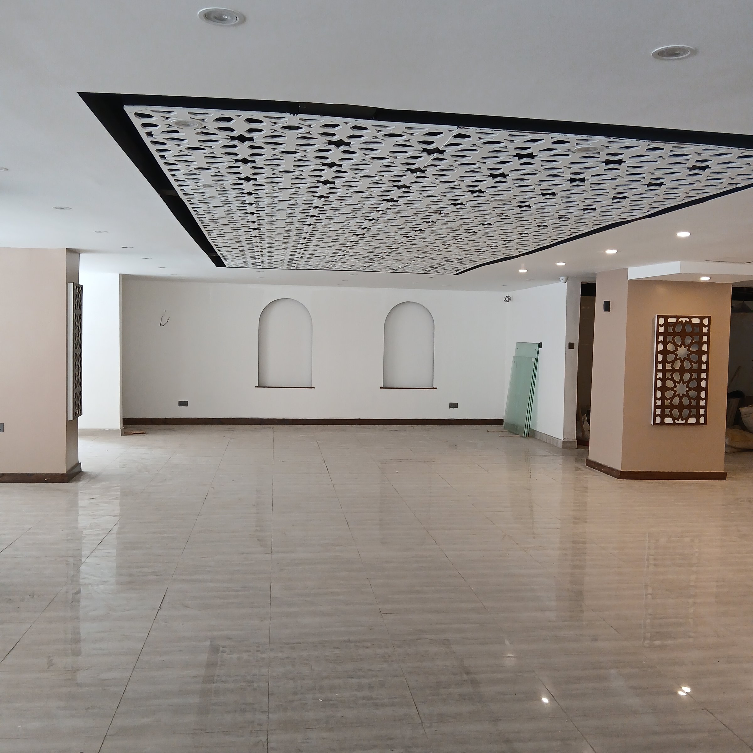 Spacious, empty room with tiled floor, white walls, decorative ceiling panels, and two arch-shaped wall niches.