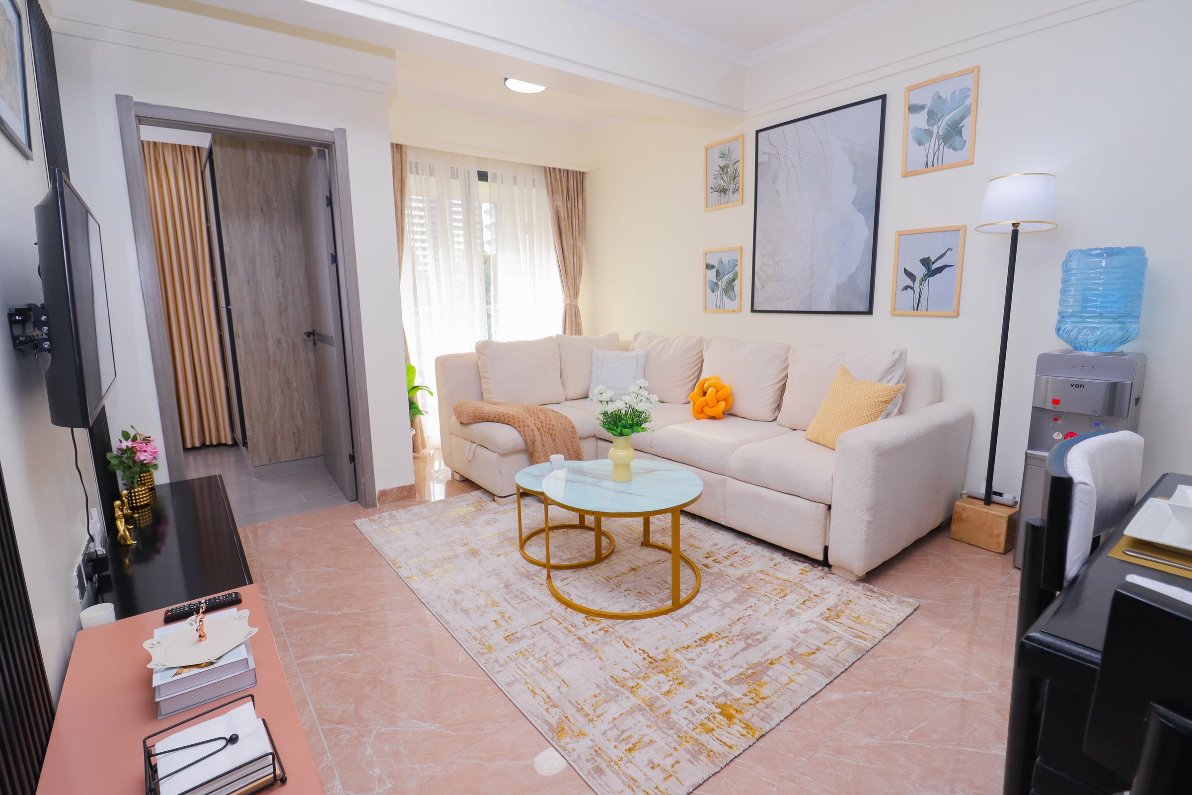 Cozy living room with a beige sofa, round glass coffee table, abstract wall art, and a water dispenser.