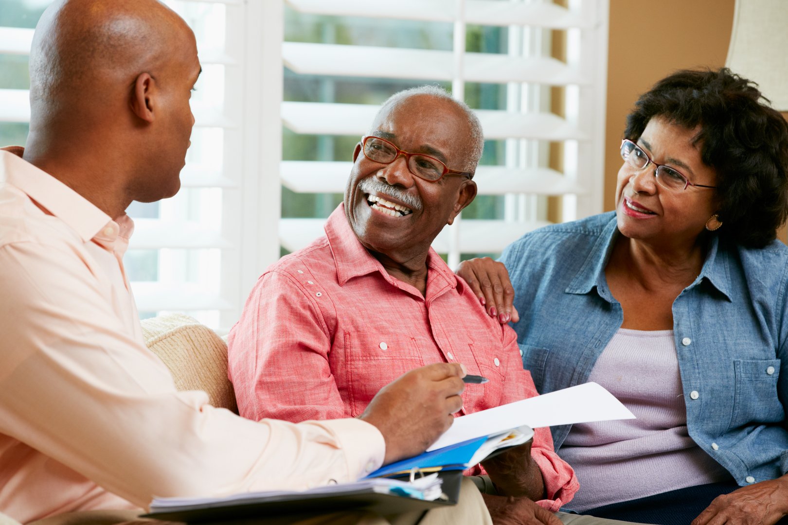 Financial Advisor Talking To Senior Couple At Home Showing Documents Smiling