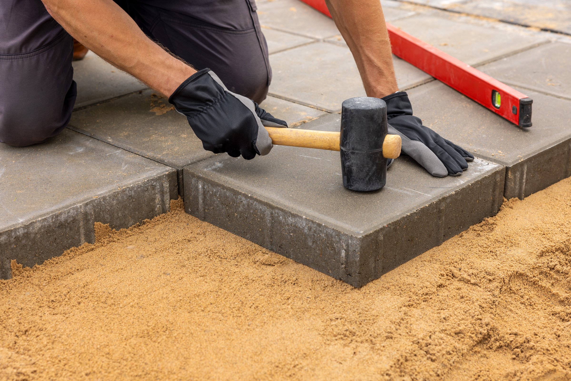 worker installing concrete paving slabs on sand foundation