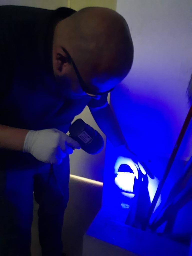 Person wearing gloves uses a UV light to inspect a surface, highlighting an area with blue illumination.