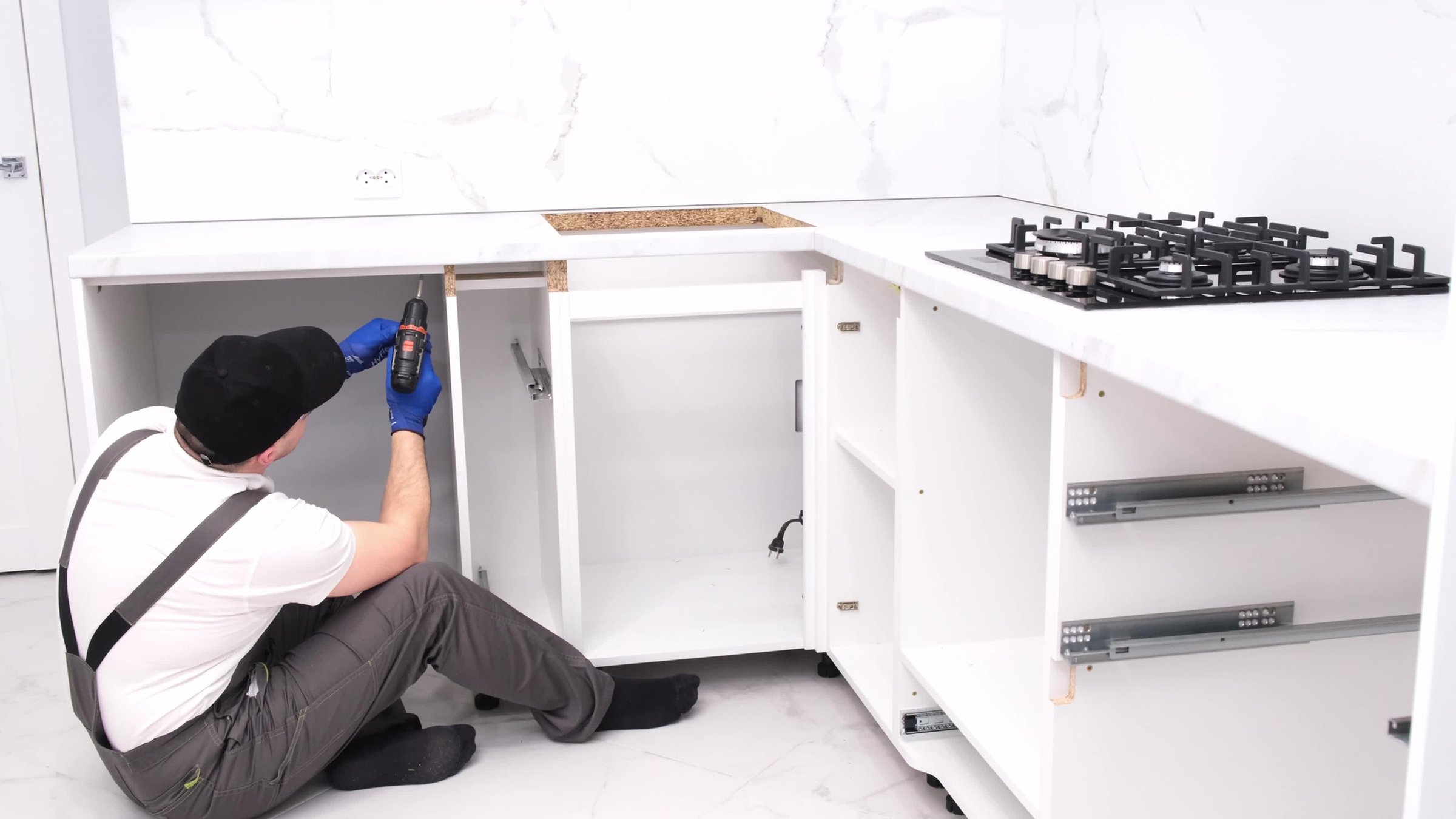A craftsman in a black cap assembles furniture in the kitchen. New kitchen in white colors.