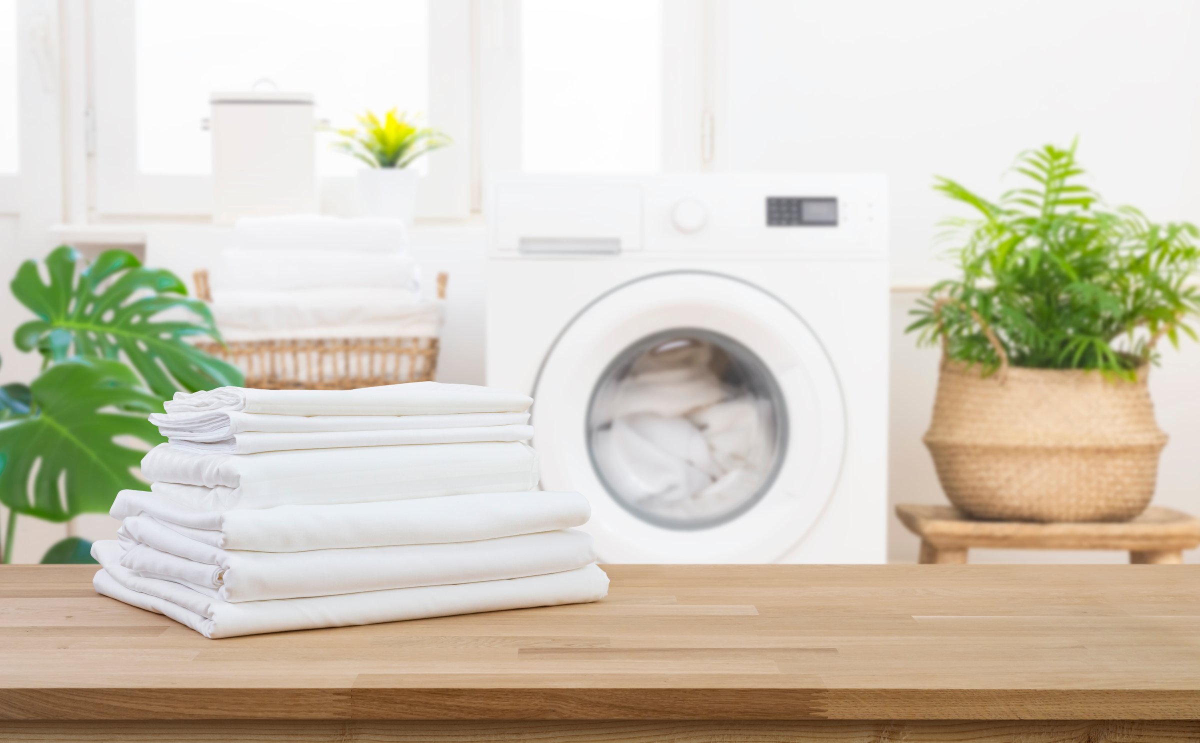 Stack of clean folded laundry bedding sheets on wooden table in blurred bathroom interior