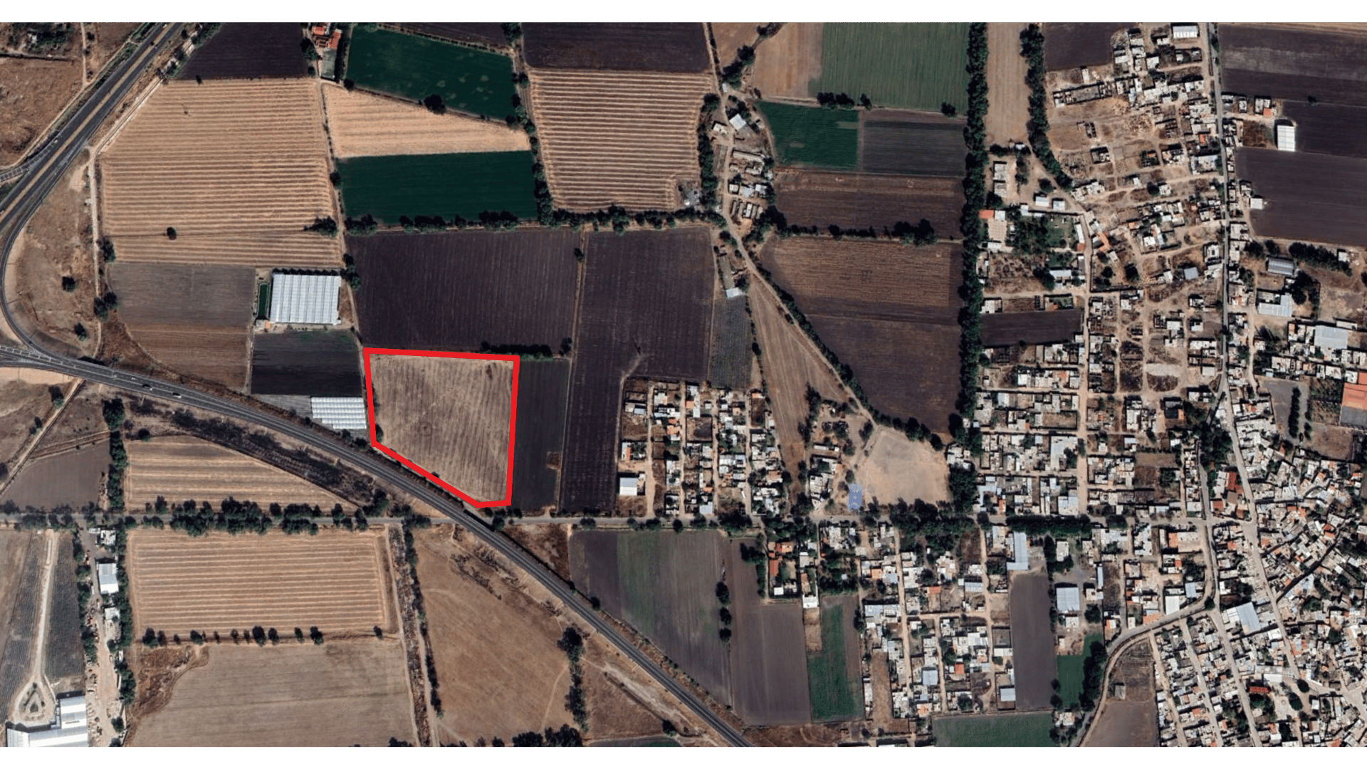 Aerial view of farmland with a red border highlighting a specific rectangular plot, surrounded by roads and a residential area.