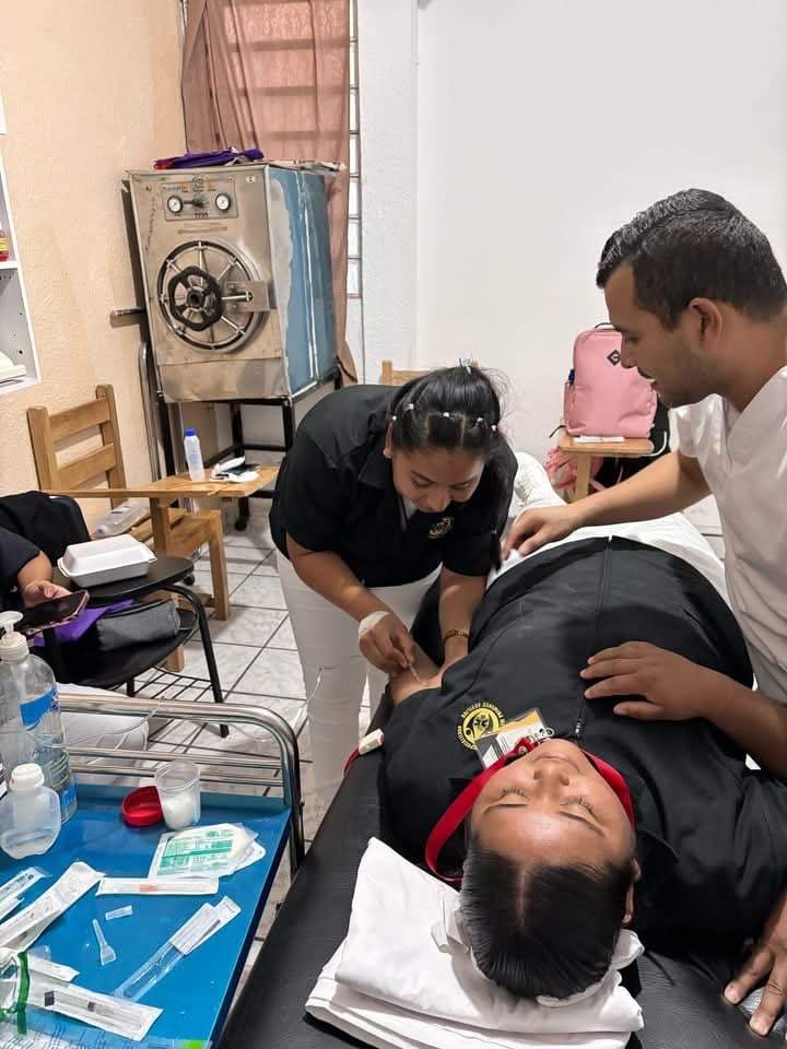 Medical staff administers treatment to a patient lying on a bed in a clinic with medical supplies nearby.