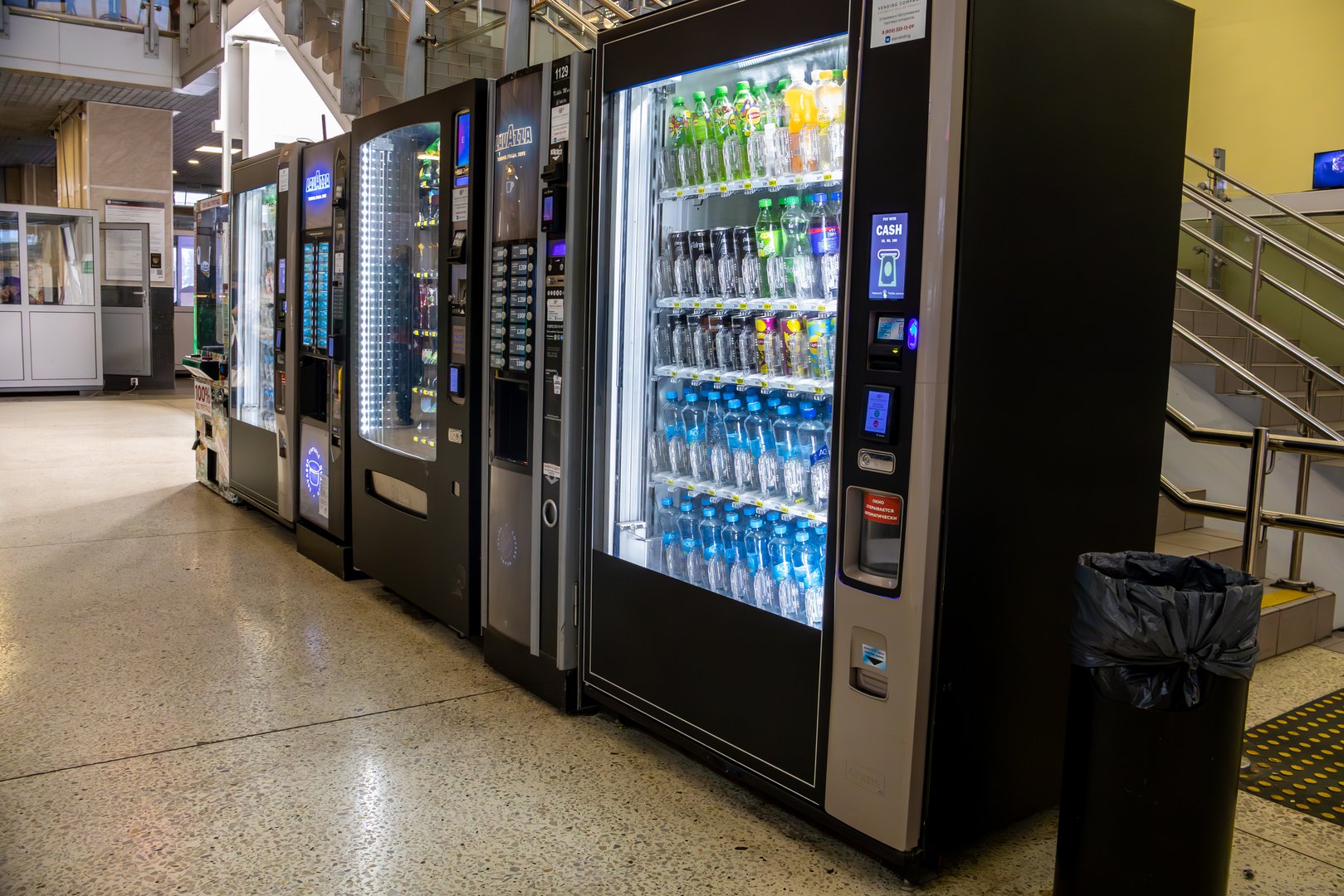 Row of vending machines with a water dispenser in the middle. The vending machines are black and silver