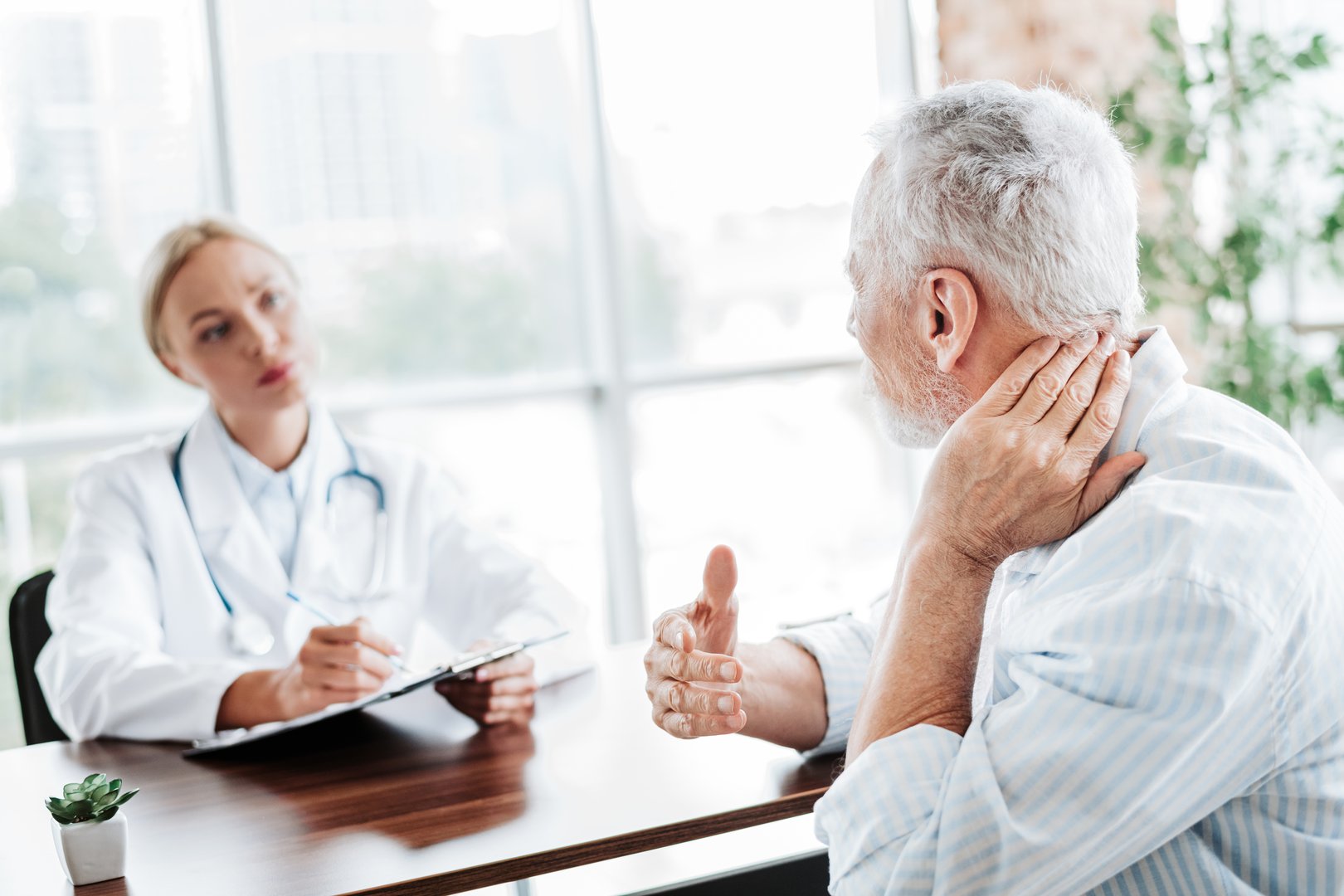 A senior male patient consulting a female doctor about neck pain in a modern and bright medical clinic