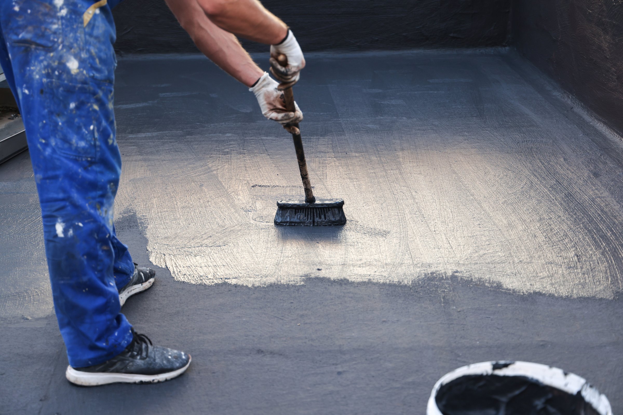Construction worker with brush applying waterproofing layer coating on a building roof