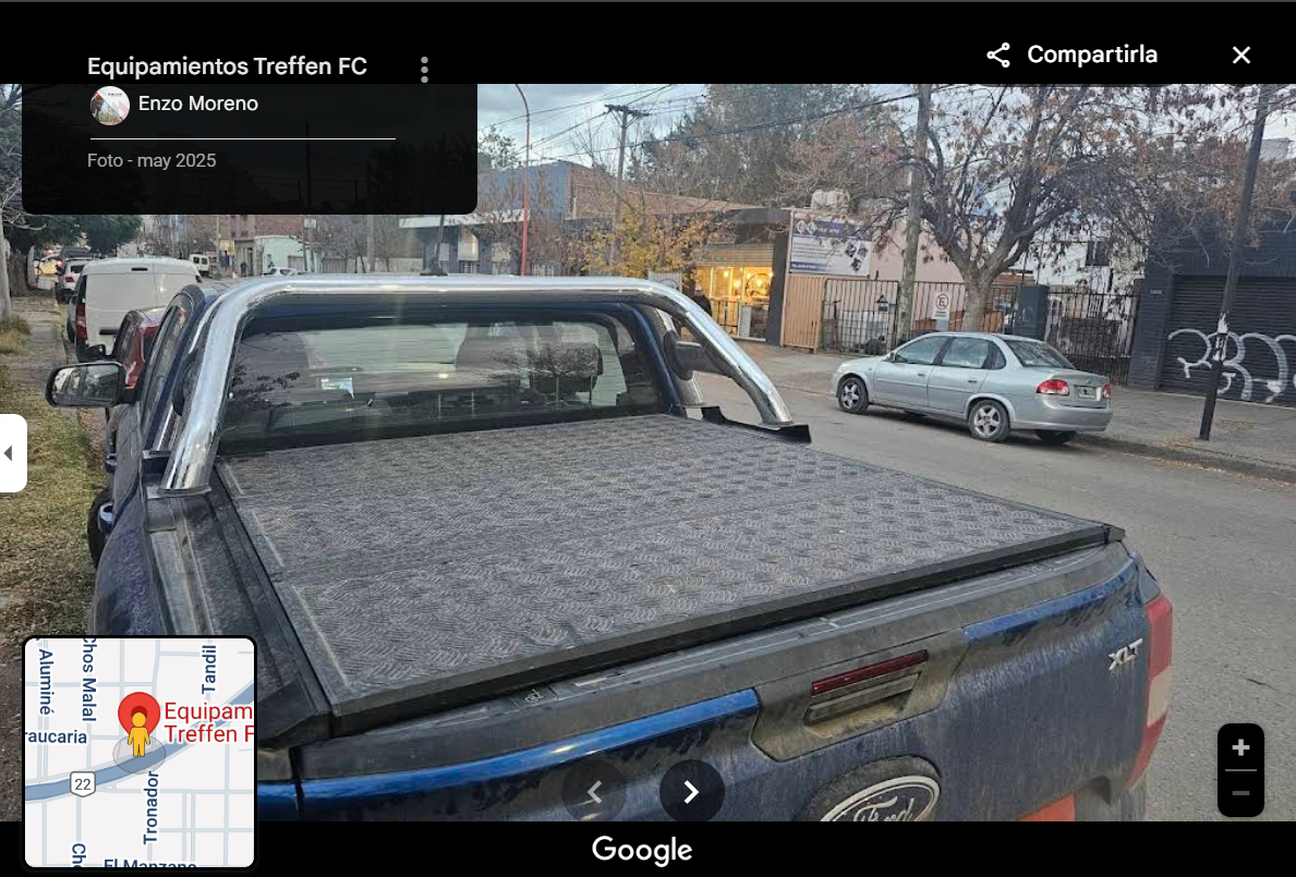 A blue pickup truck with a covered bed parked on a suburban street with other cars and trees in the background.